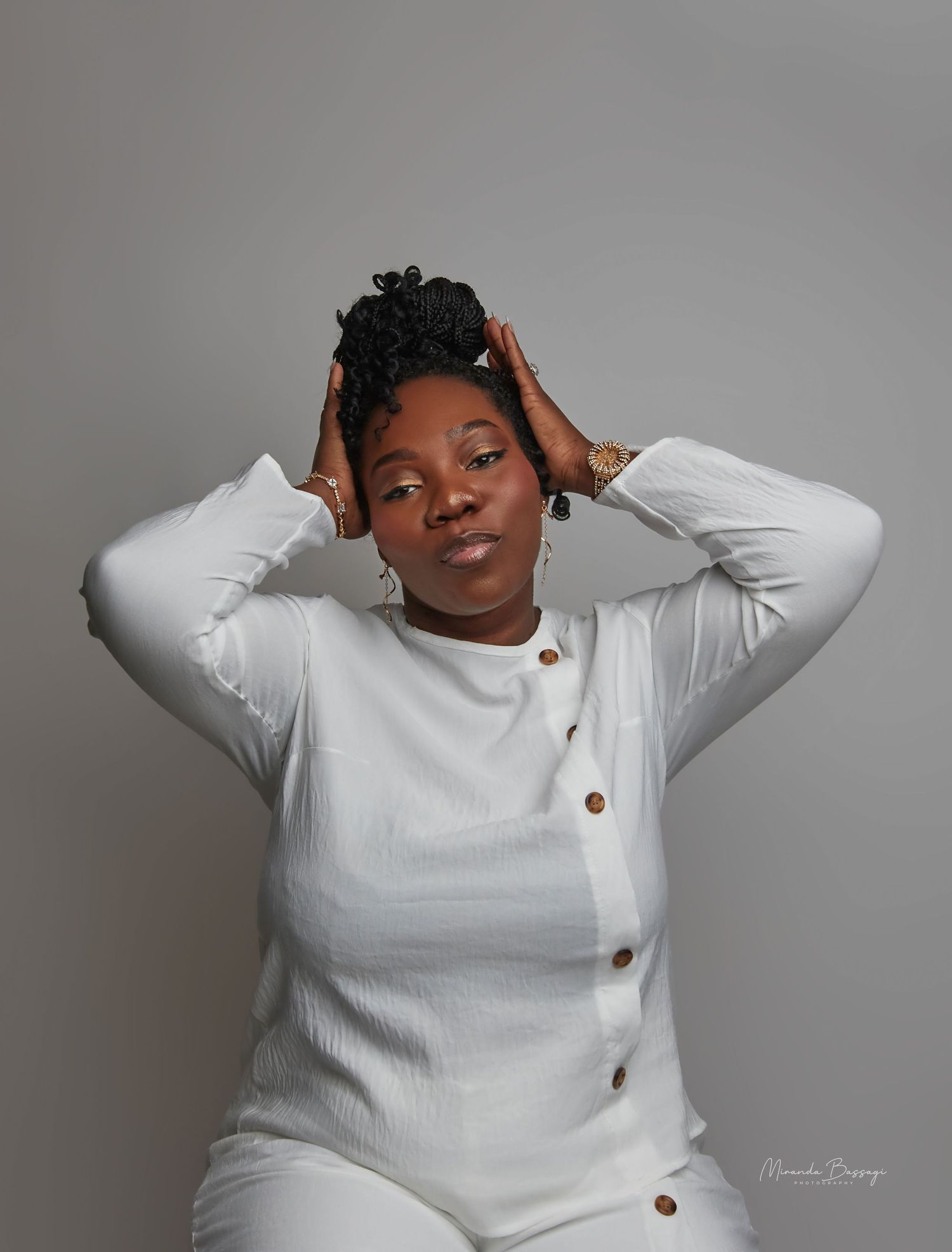 Model poses in white sweater with brown buttons against grey background in fashion photoshoot series.