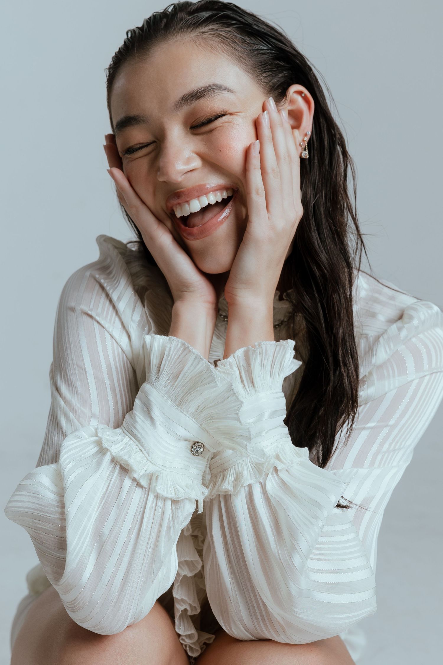 Joyful portrait in white ruffled blouse with hands on cheeks displaying genuine laughter.