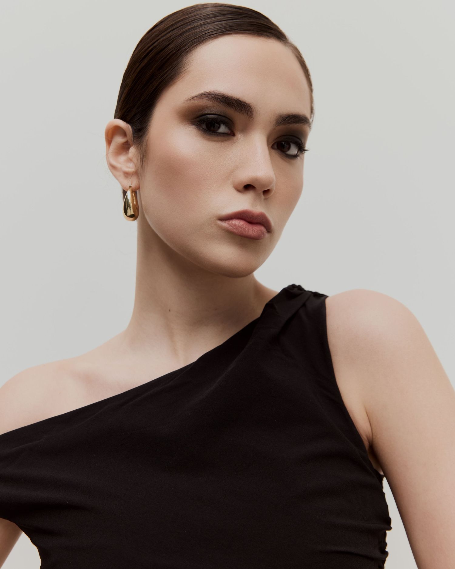 Fashion model in elegant black one-shoulder dress poses against neutral background for high-end editorial shoot.