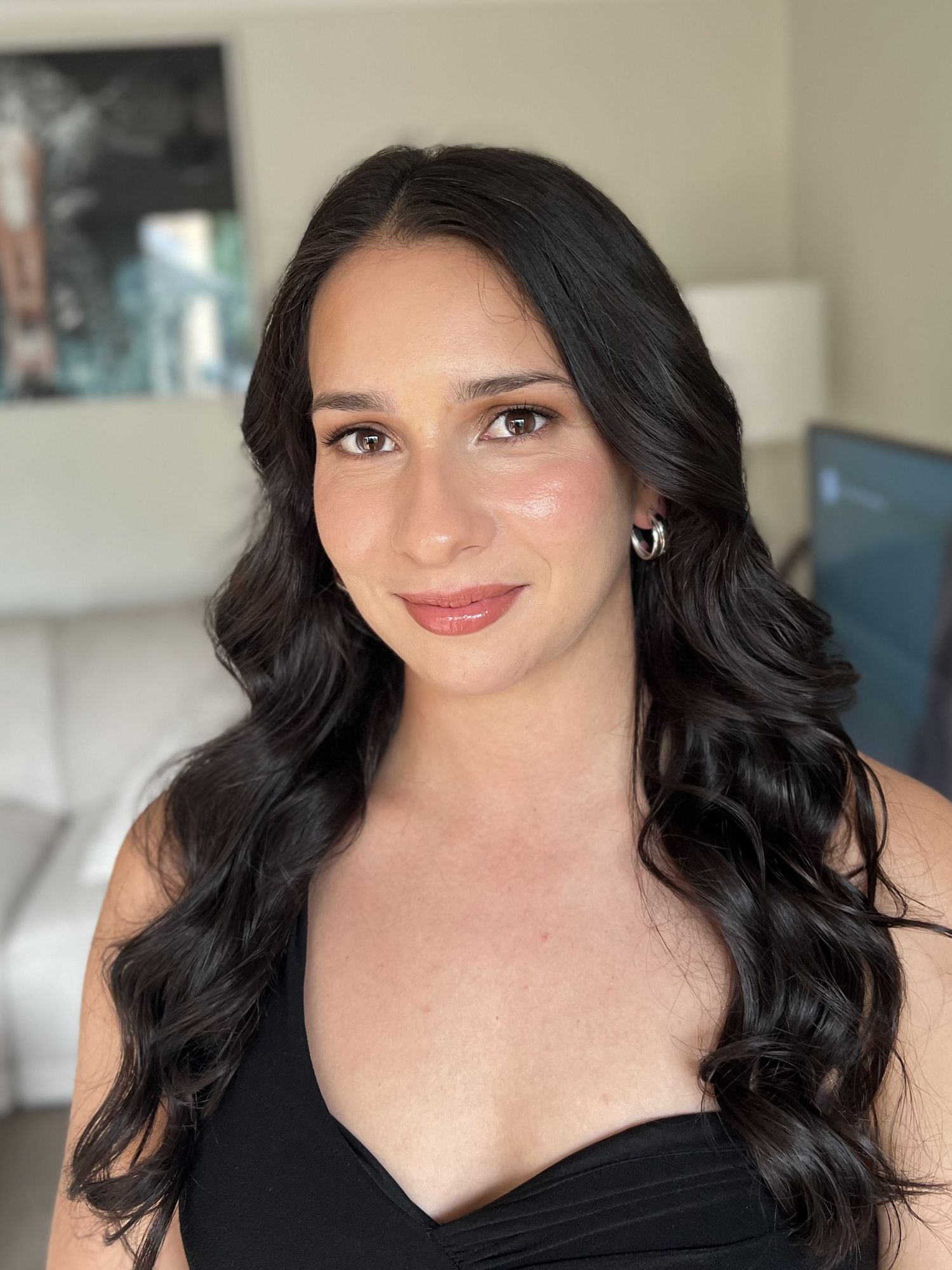 Portrait of someone with dark wavy hair wearing a black top against a light background.