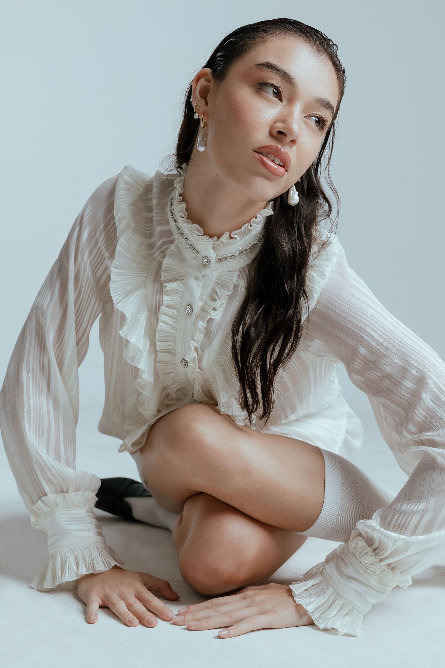 Model in vintage-inspired white ruffled blouse poses gracefully on minimalist white background.