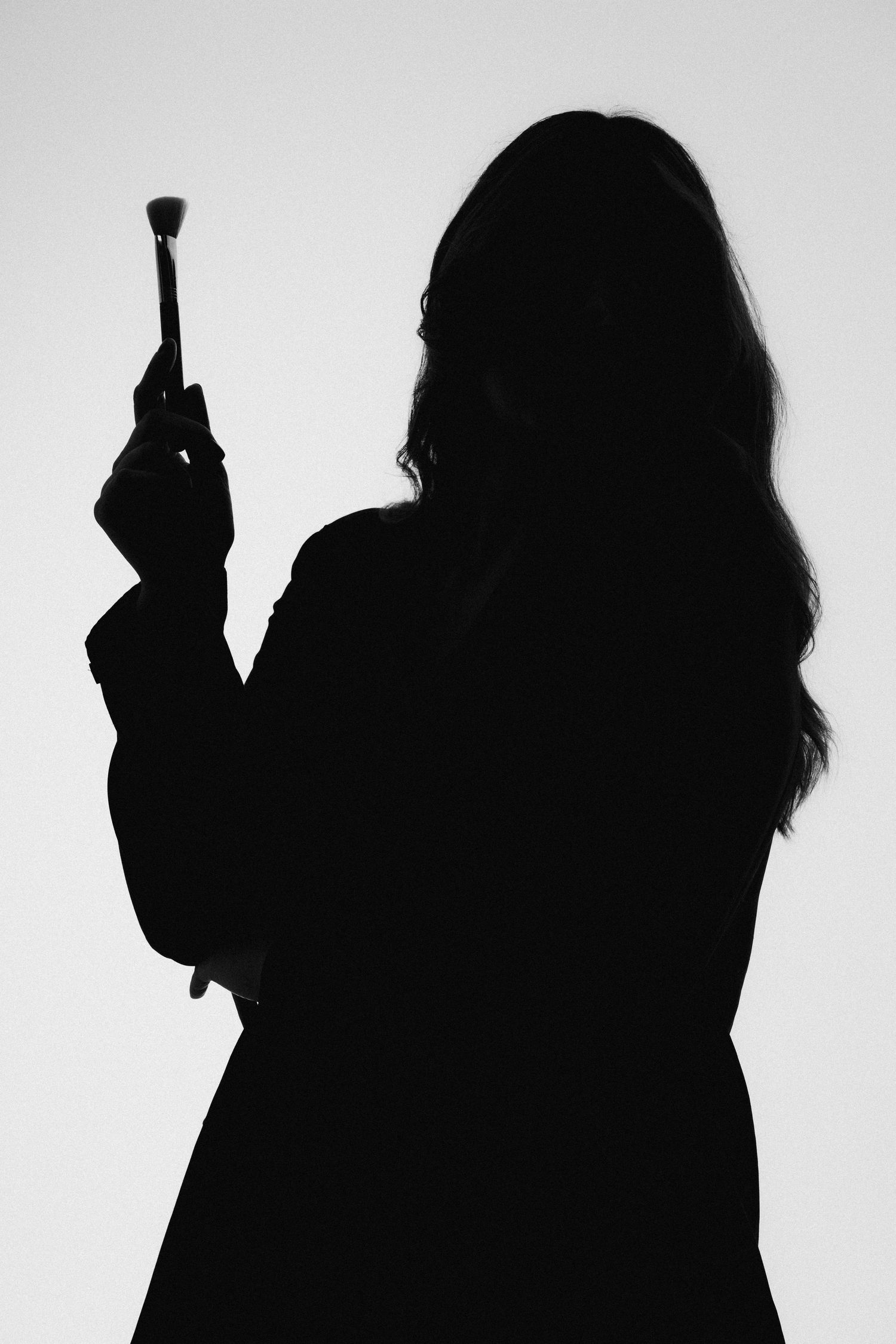Silhouetted figure with beauty brushes against white background.