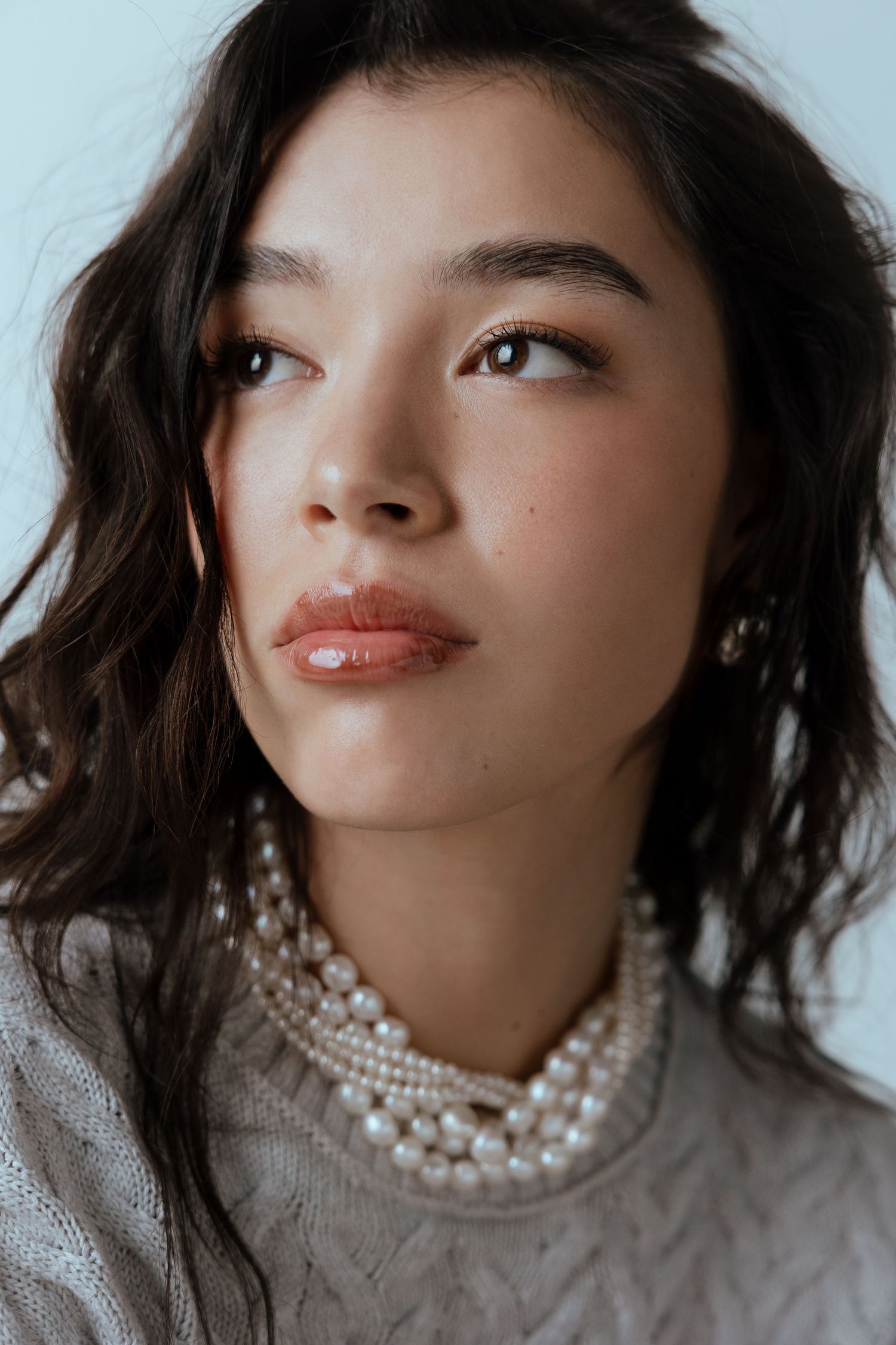 Elegant beauty portrait featuring pearl necklace and cable knit sweater against light backdrop.