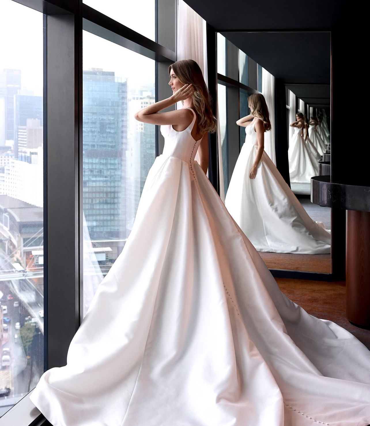 Elegant wedding dress with full skirt photographed against modern cityscape with mirror reflections.