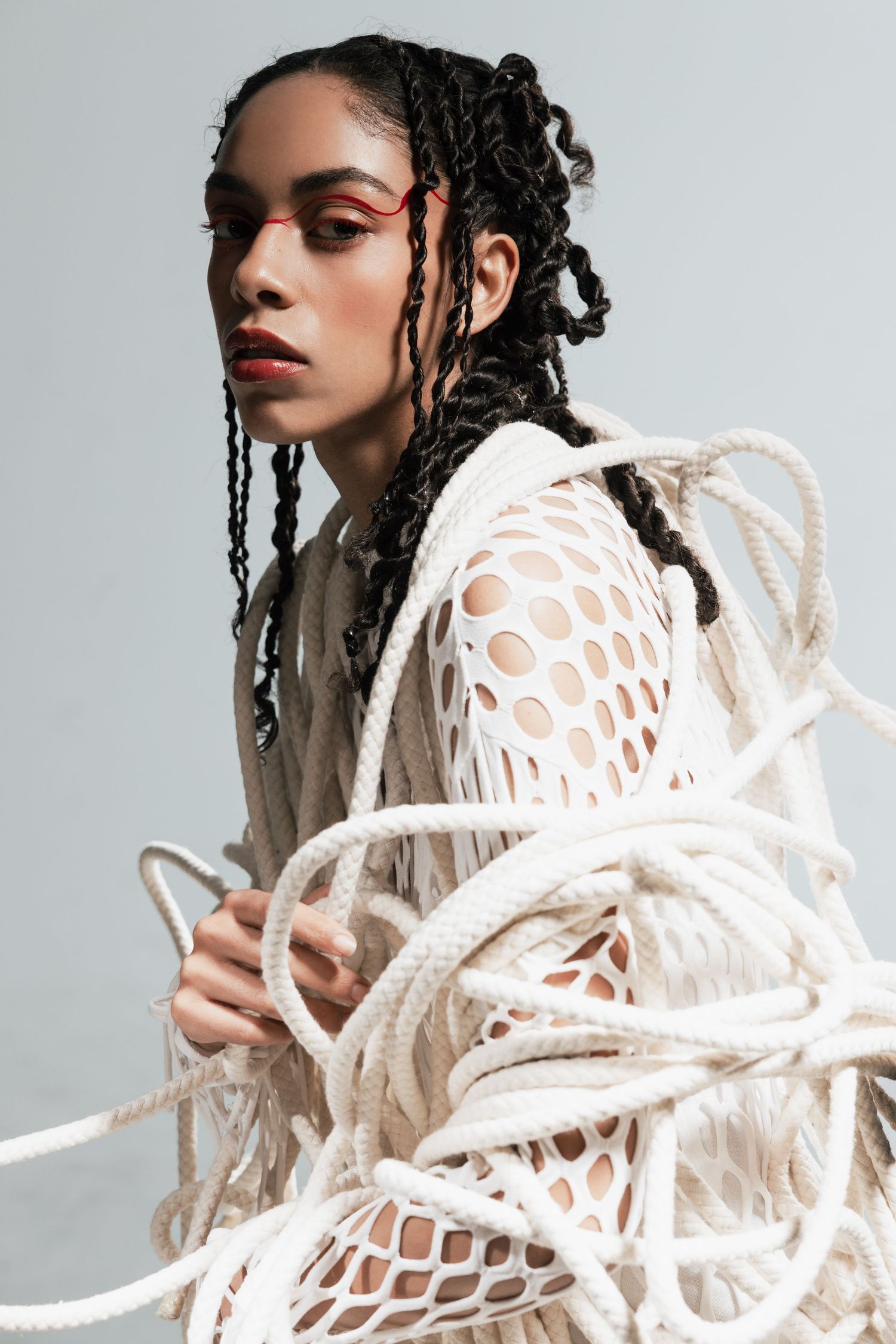 Fashion portrait with braided hair and white sculptural woven sweater against neutral backdrop.