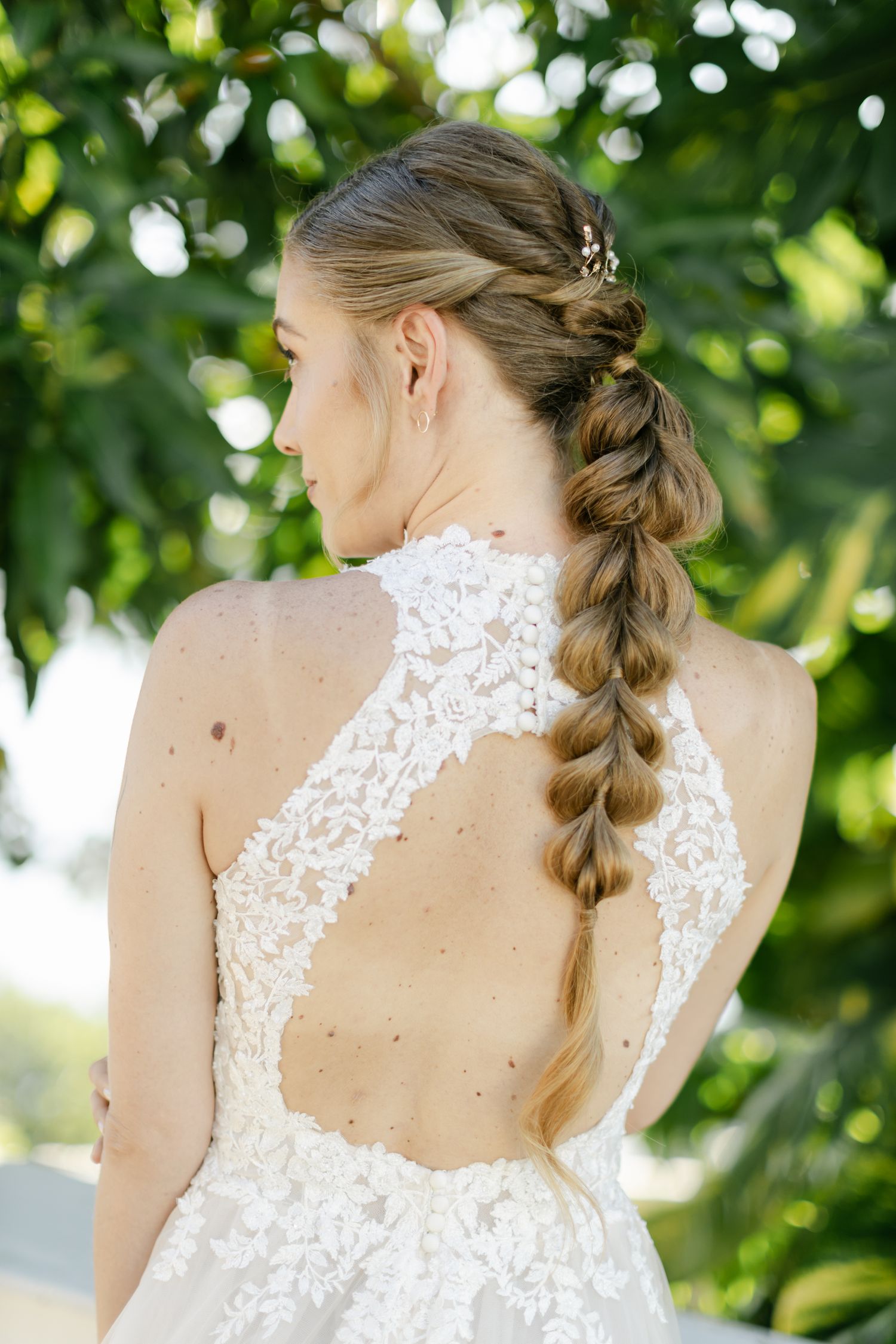 Intricate lace detail on back of white wedding gown shown in outdoor garden setting.