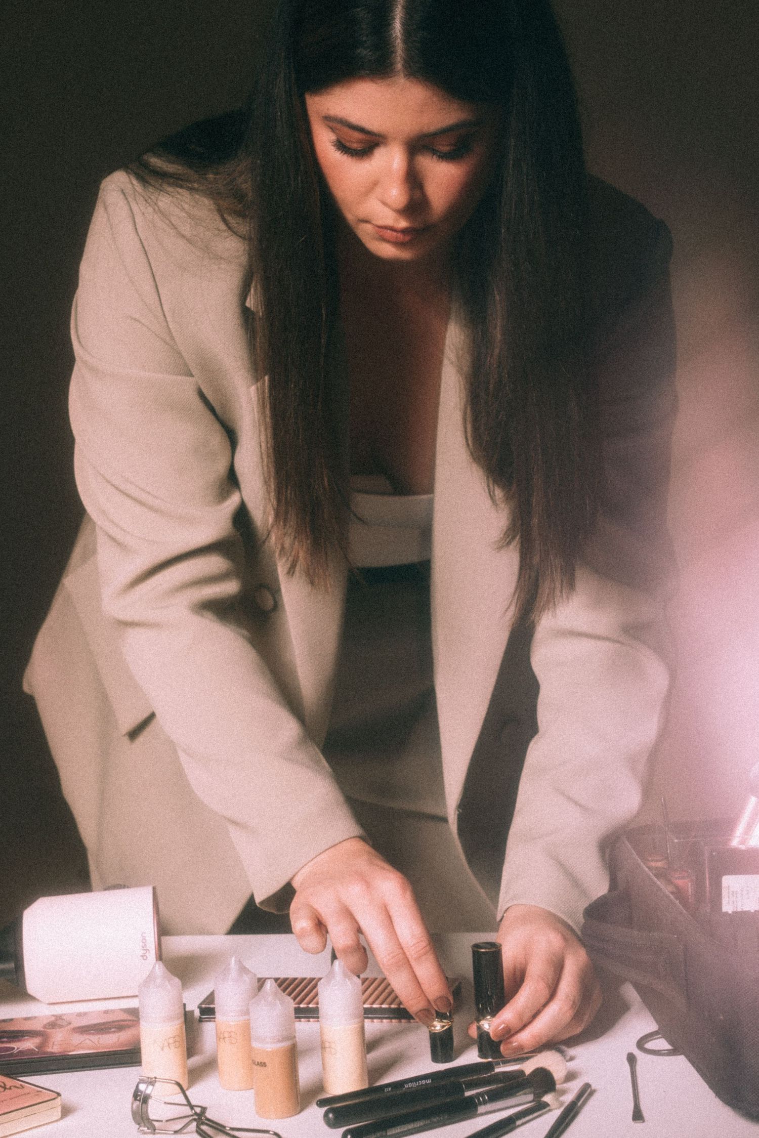 A series of close-up shots showing hands working with makeup products and tools in warm lighting.