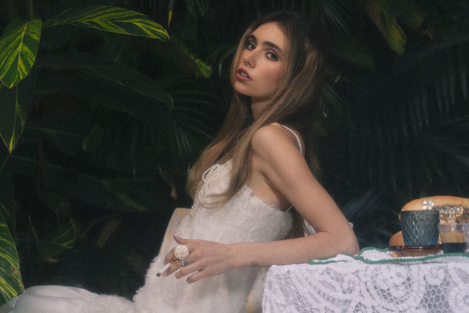 A dreamy outdoor portrait in a white dress against lush tropical foliage with a vintage tea setting.