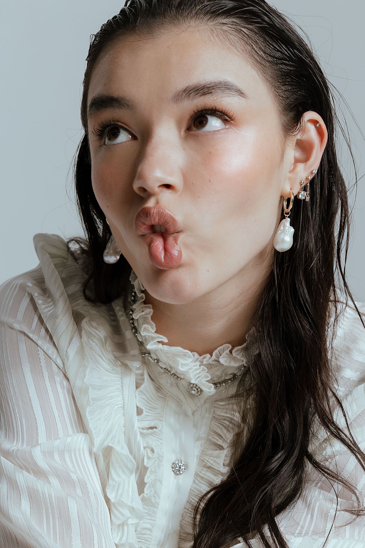 Playful portrait in white ruffled blouse with pearl drop earrings making kissing expression.