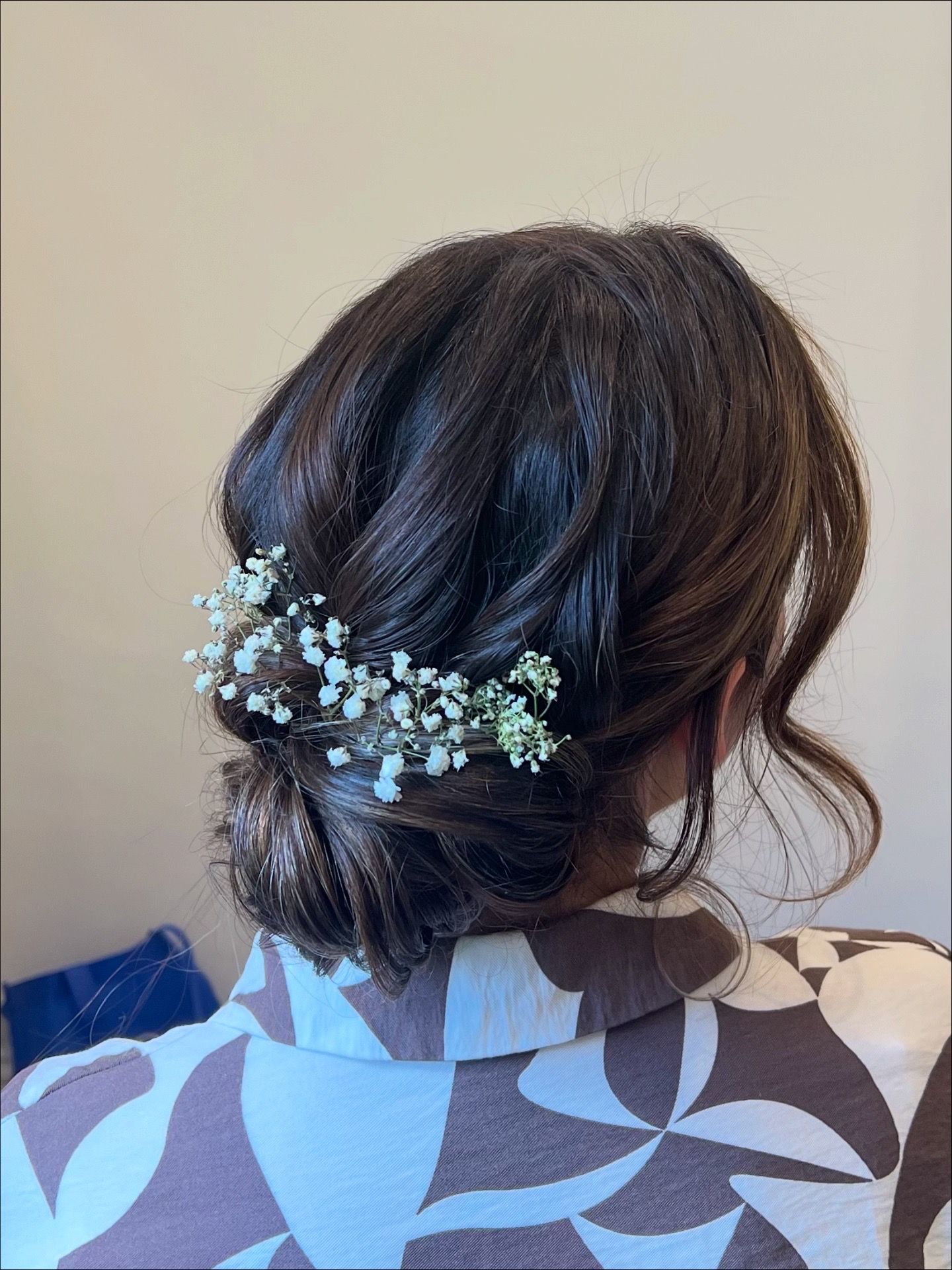 A delicate floral hair accessory with small white baby's breath flowers adorns a brunette updo hairstyle.