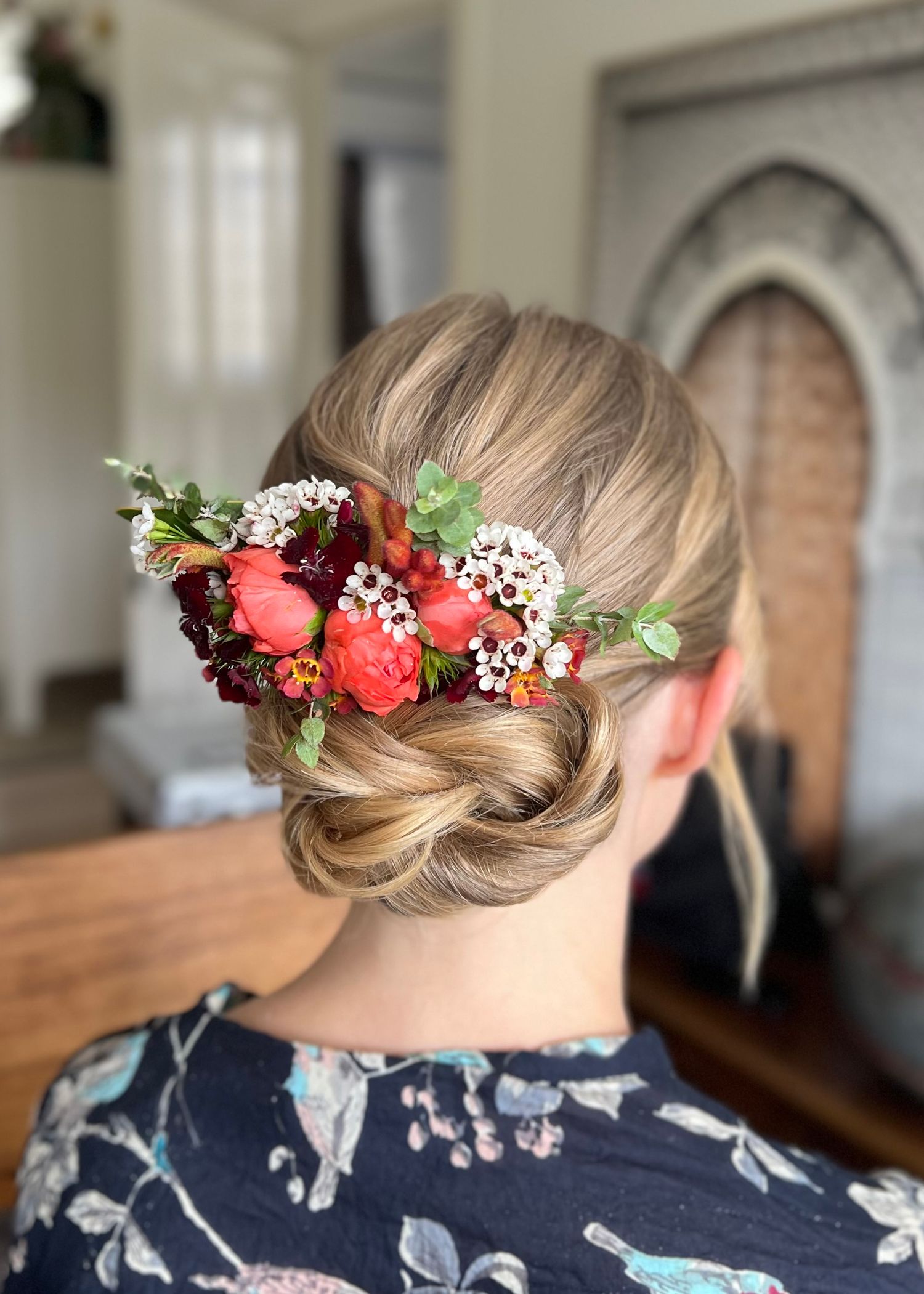 Elegant bridal updo adorned with red and white flowers and greenery.