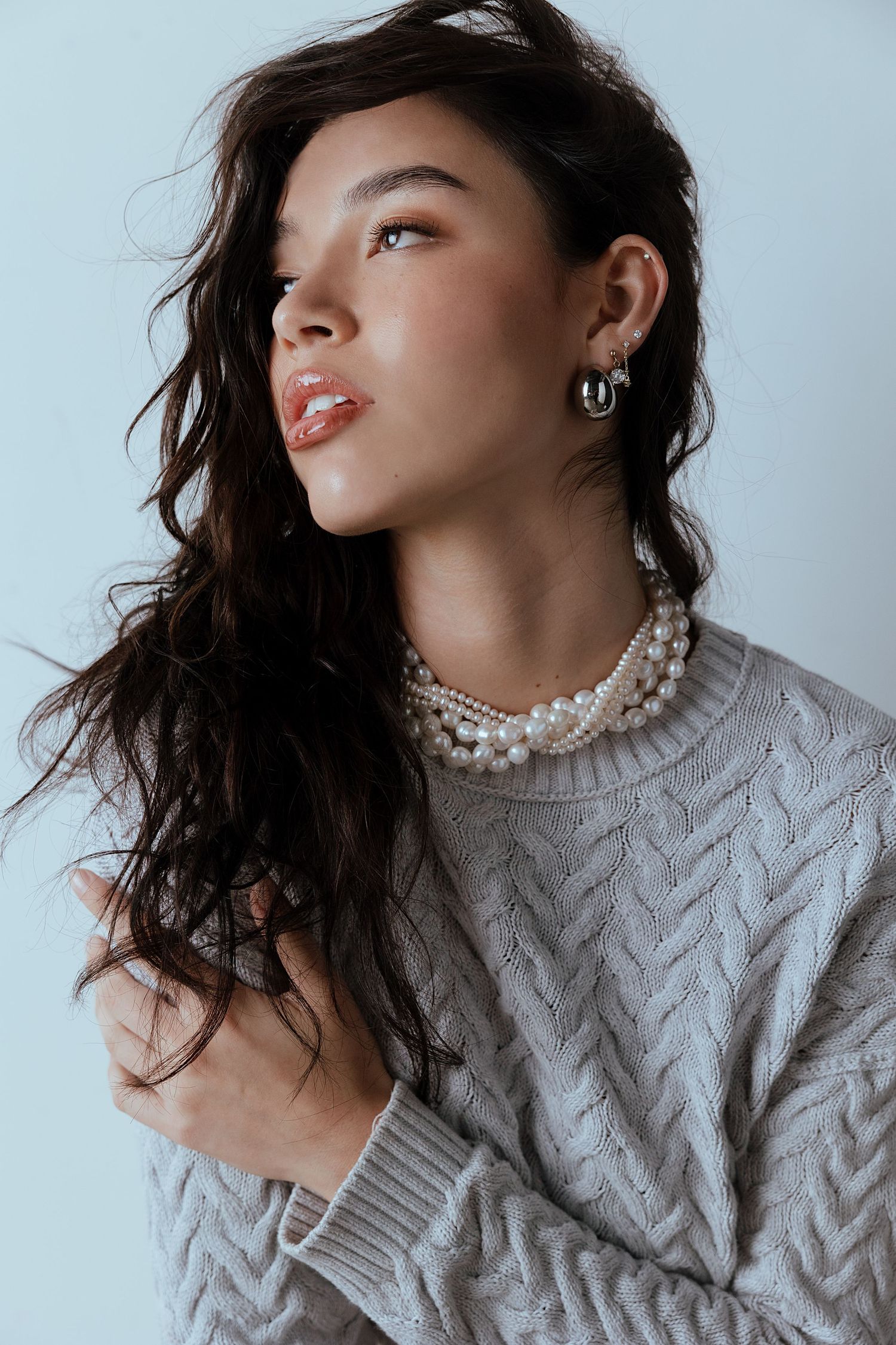 Fashion portrait showcasing cable knit sweater and layered pearl necklace against light background.
