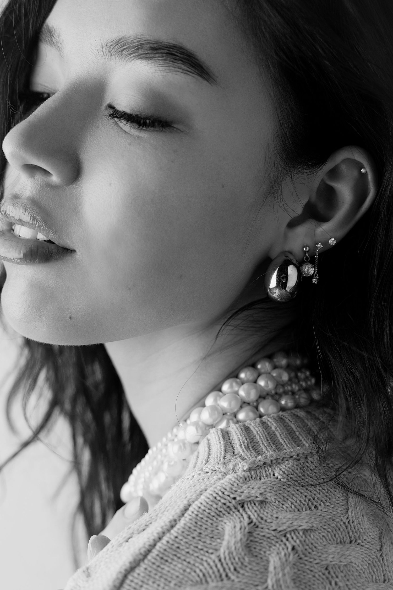 Artistic black and white profile shot featuring pearl necklace and delicate earrings.