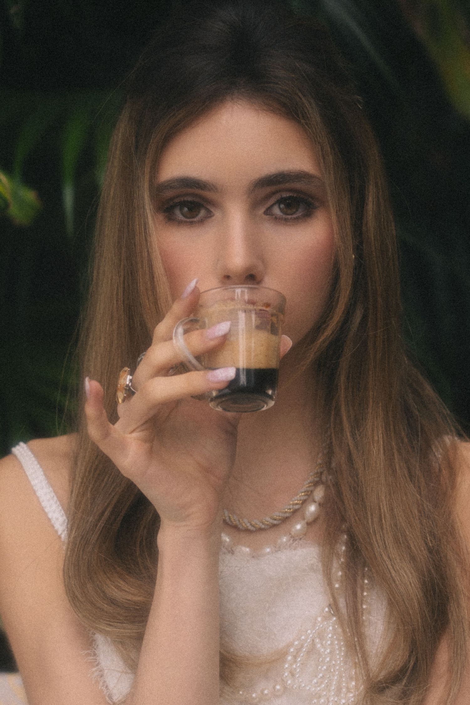 A person in a white lace dress sips from a delicate teacup in a garden setting.