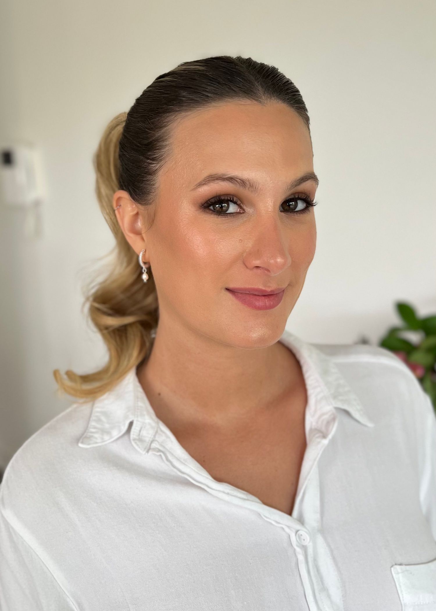 Professional makeup look with sleek ponytail and white button-down shirt.