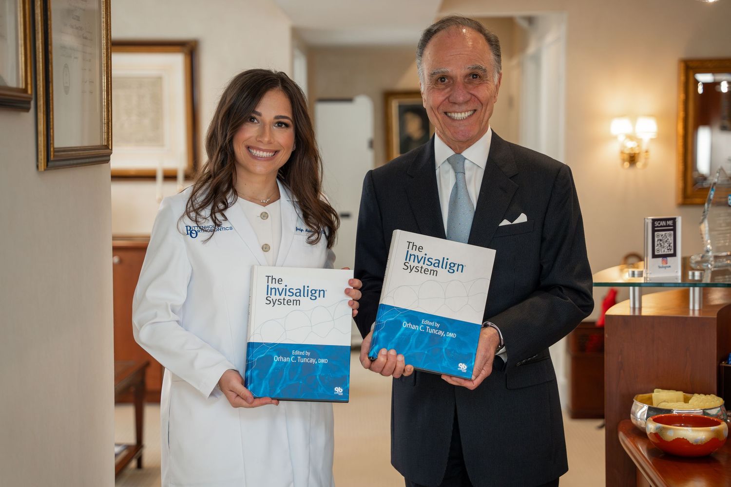 Man and woman in white coat holding The Invisalign System books indoors.