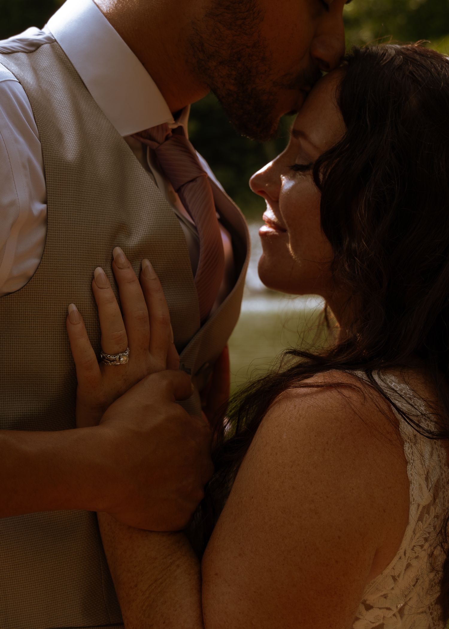 Romantic close-up of smiling bride leaning toward groom in tan suit, showing diamond engagement ring.