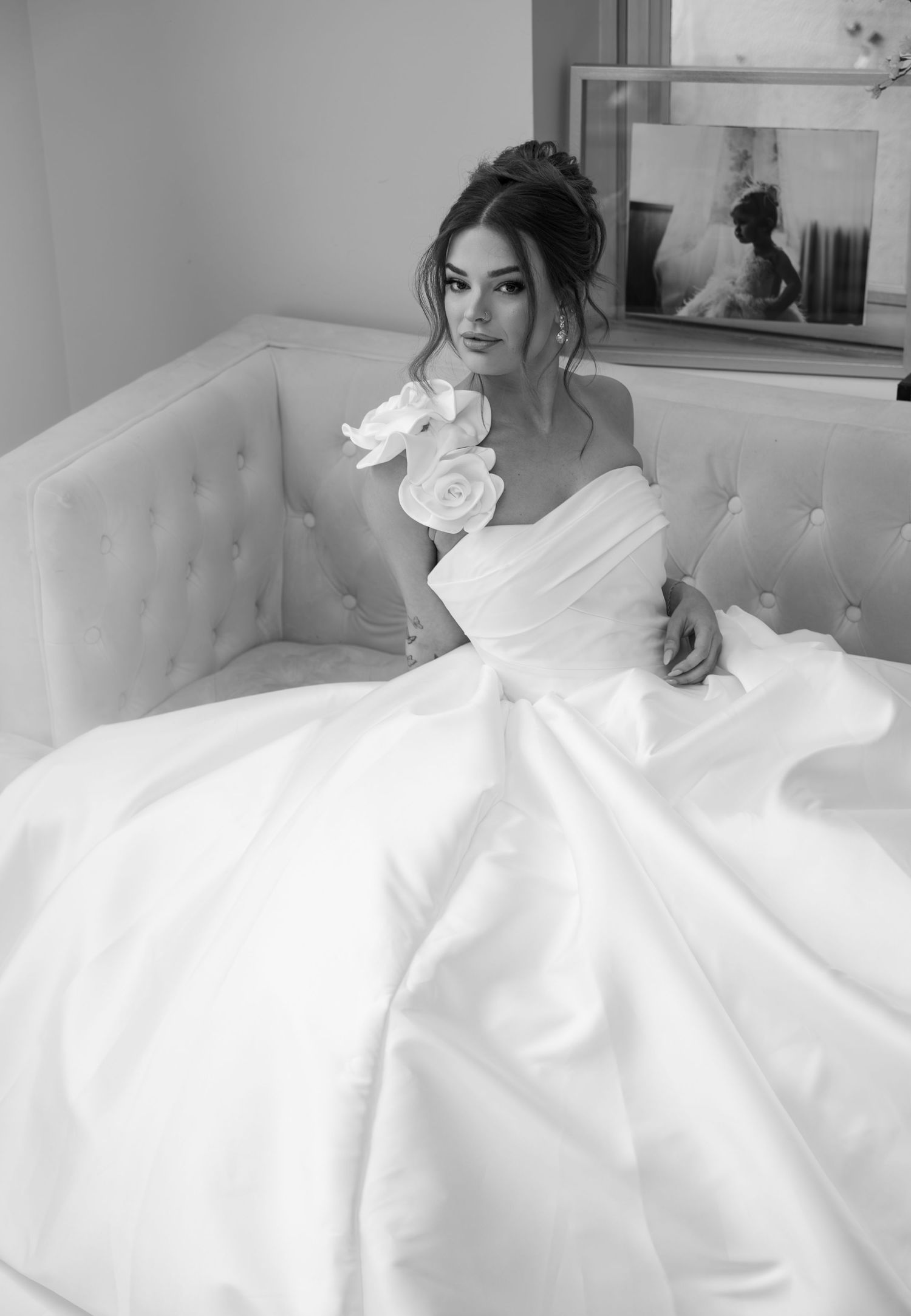 Beautiful bride in voluminous ball gown with floral detail seated on tufted sofa in black and white portrait.