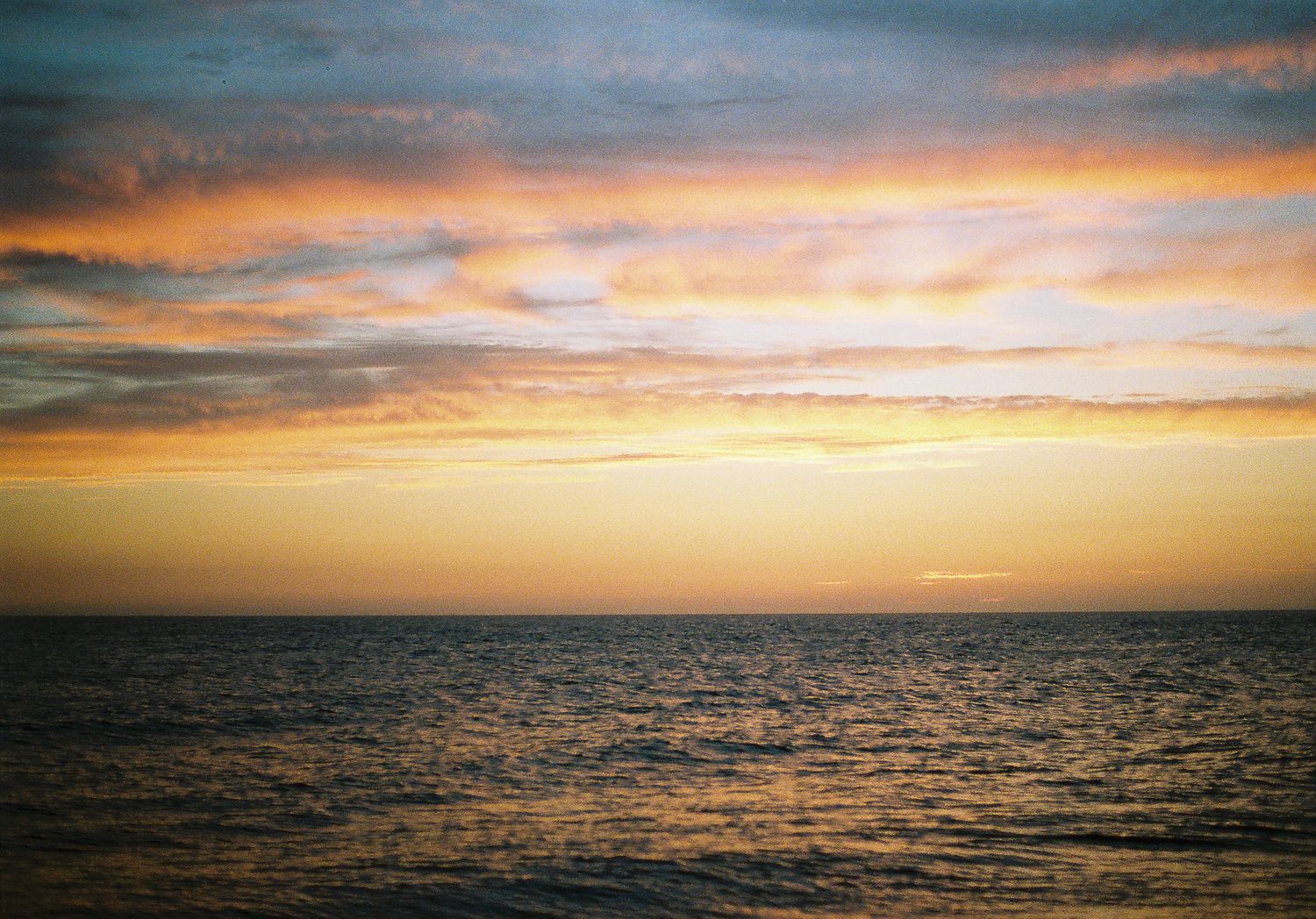 Dramatic golden sunset over calm ocean with colorful orange and blue cloudy sky.