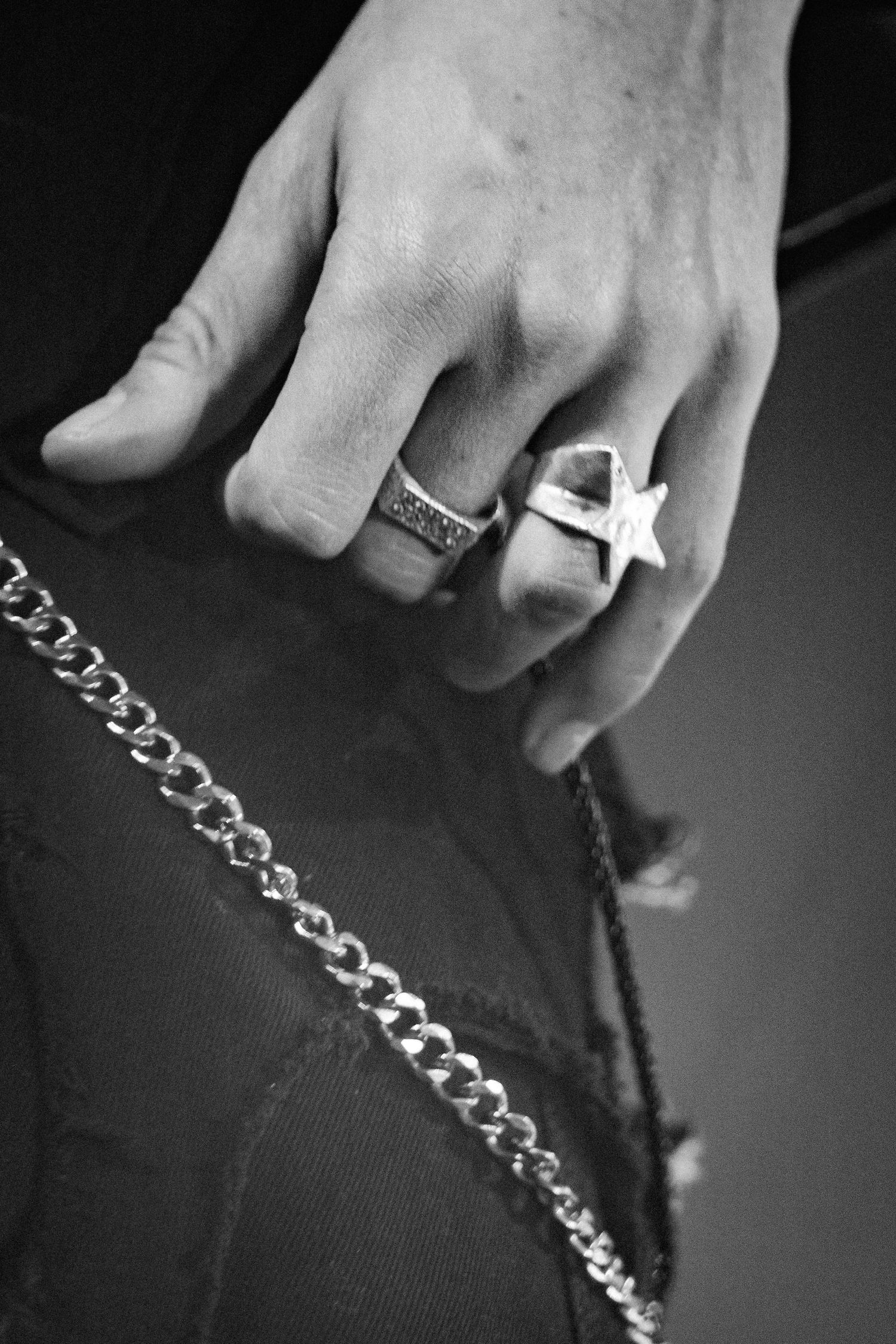 Black and white close-up of hand wearing star and band rings with silver chain necklace.