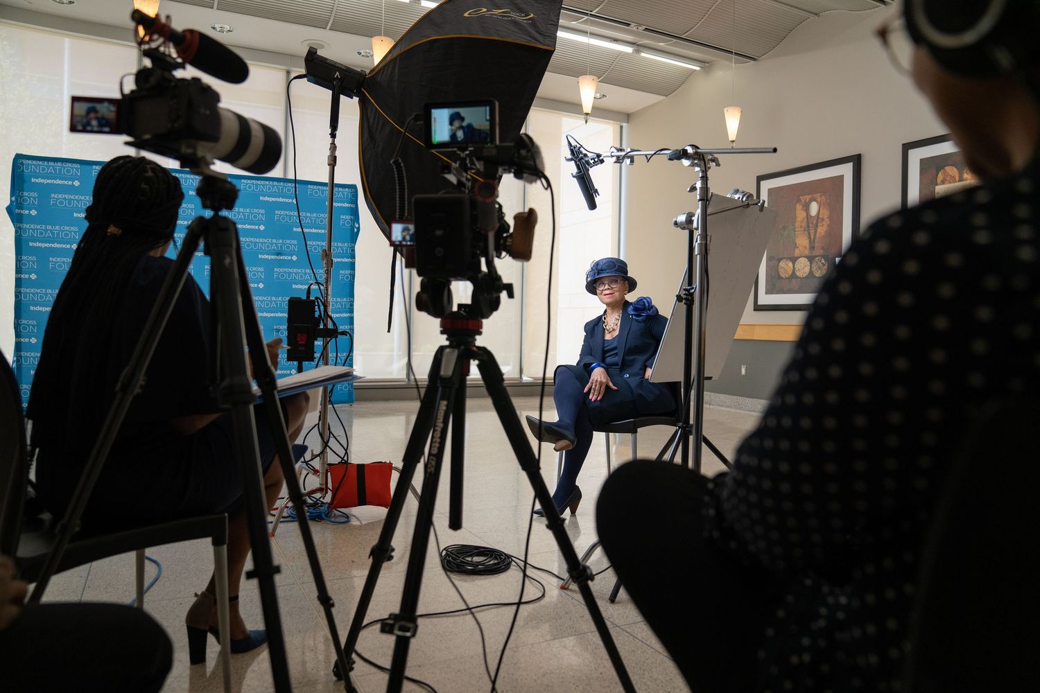 A woman in blue being filmed by a camera crew in a photography studio setting.
