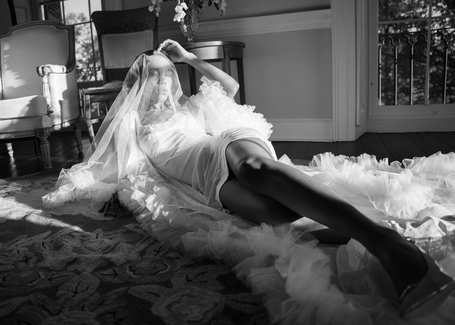 Black and white bridal boudoir photo of bride in tulle dress and thigh highs on ornate floor.