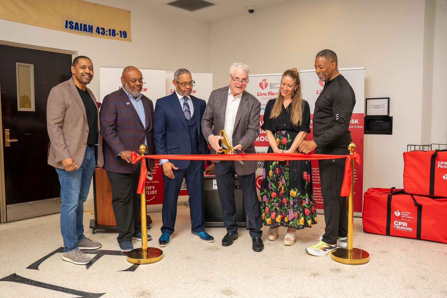 Group of six people cutting a red ribbon at a new CPR kiosk unveiling at a church.