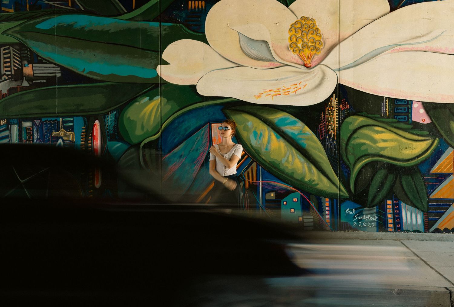 Colorful street mural featuring large white magnolia flower with city skyline background.