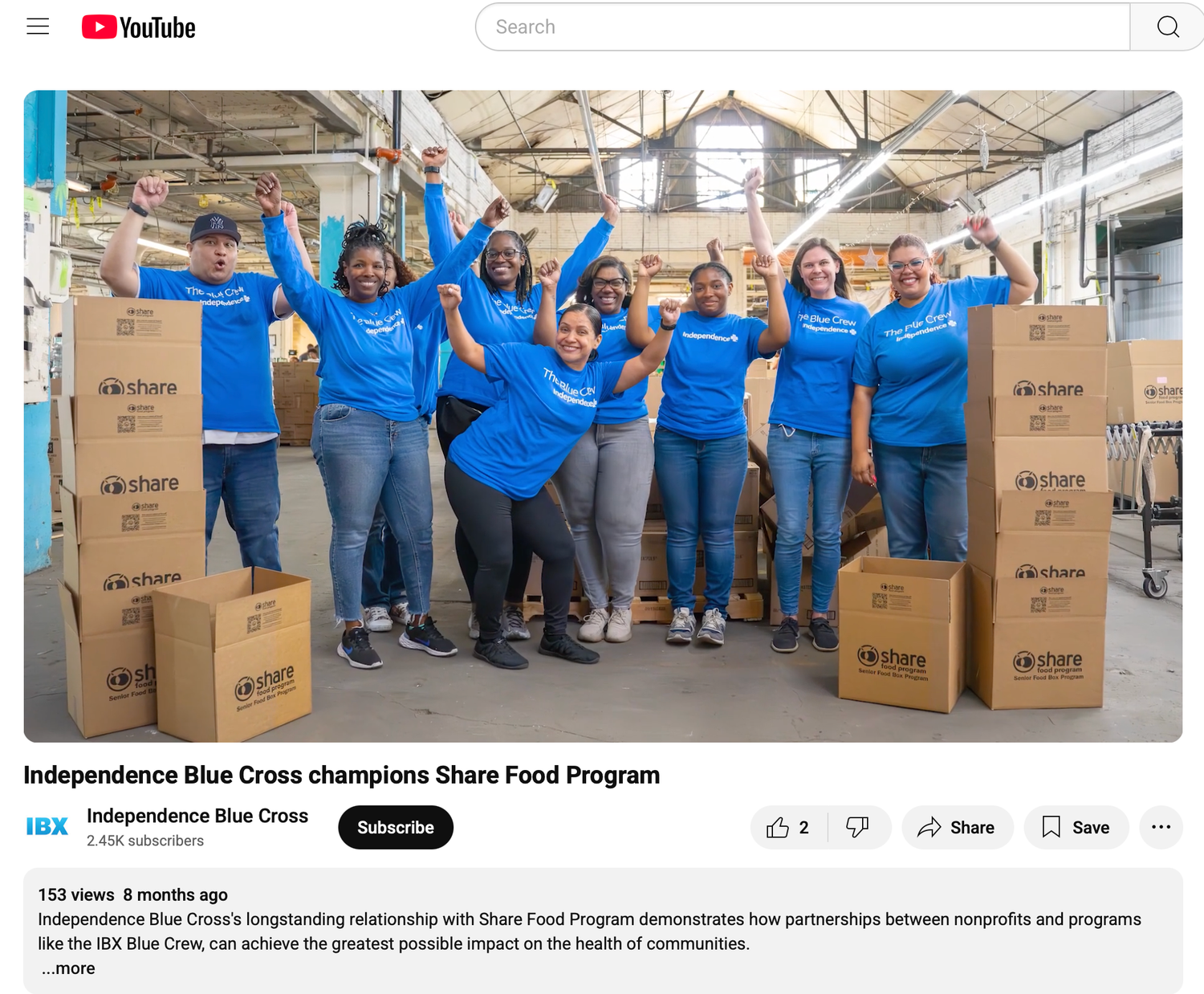Group of volunteers in blue Independence Blue Cross shirts smiling with donation boxes in a warehouse.