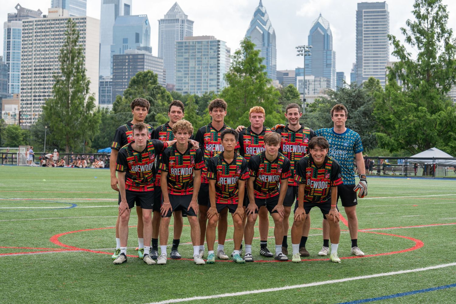 Sports team posing together on a green field with Philadelphia city skyline in the background.