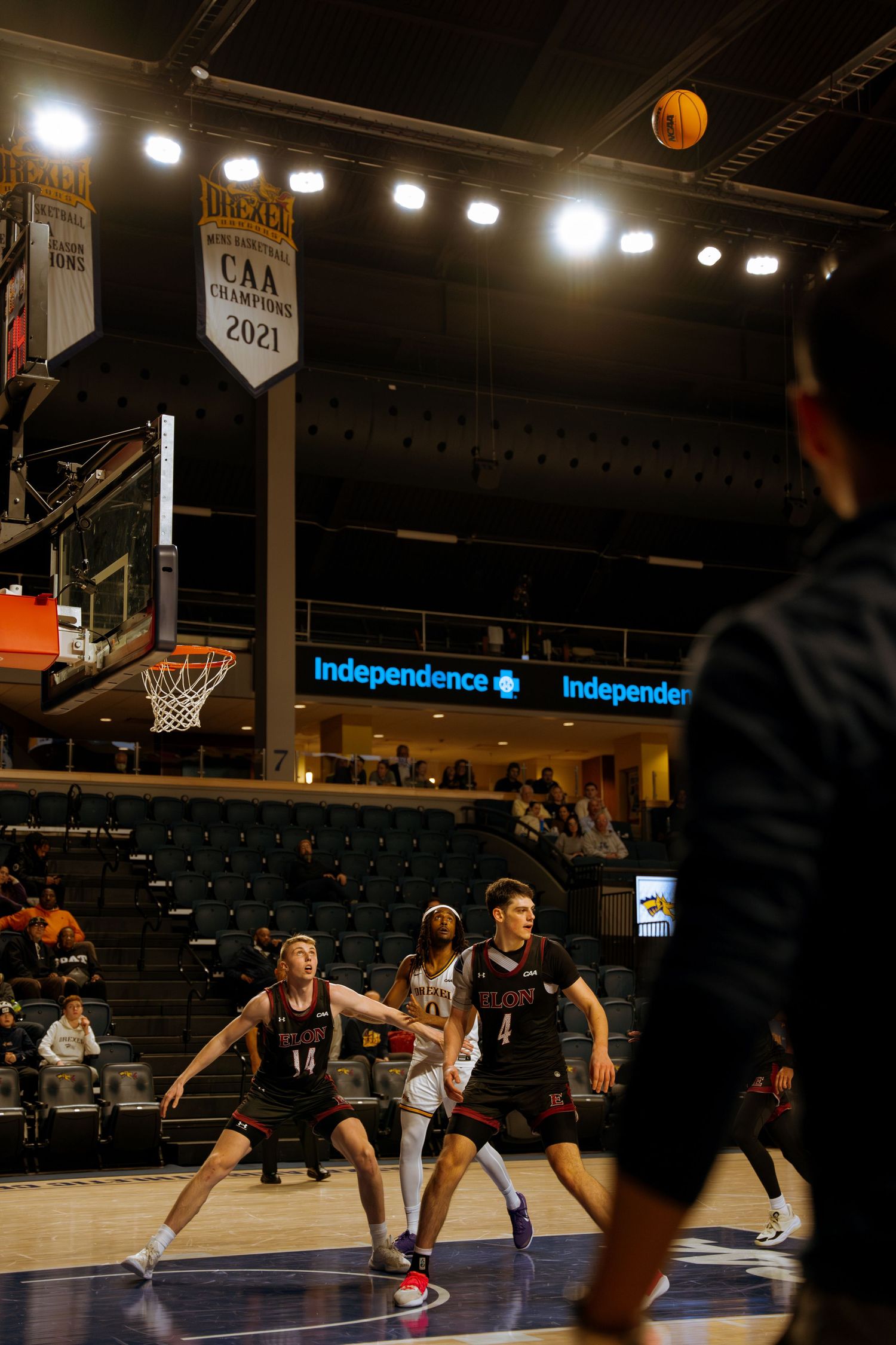 College basketball players position under hoop during game in arena displaying CAA Champions 2021 banner.