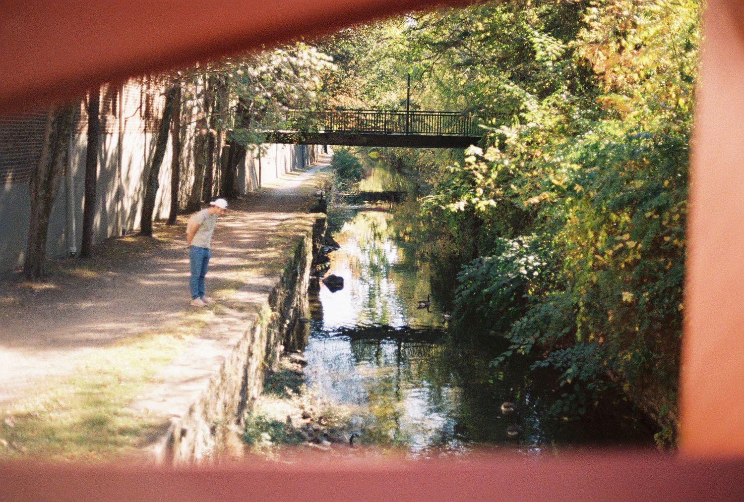 A person walking along a historic stone canal path with a bridge reflected in the water.