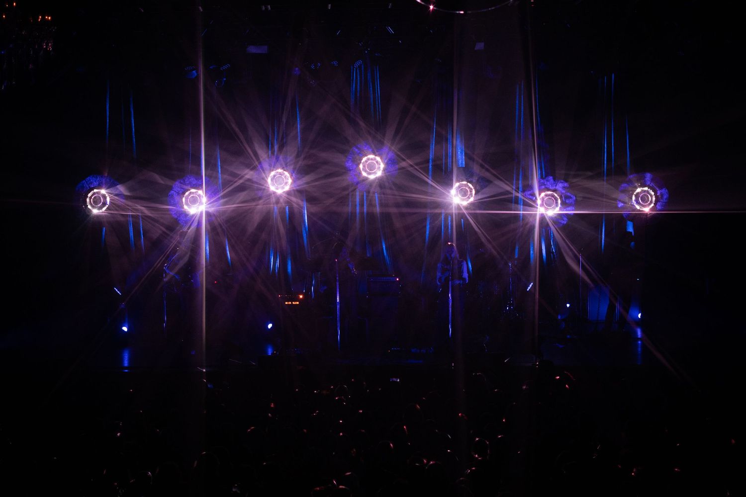 Dramatic concert stage lighting with six bright starburst lights against a dark background.