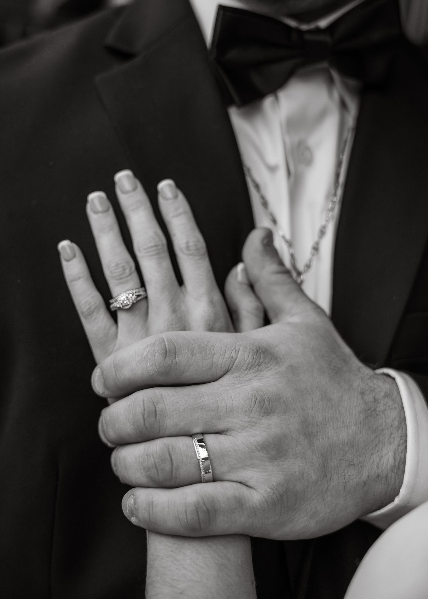 Black and white close-up of bride and groom's hands showing wedding rings.