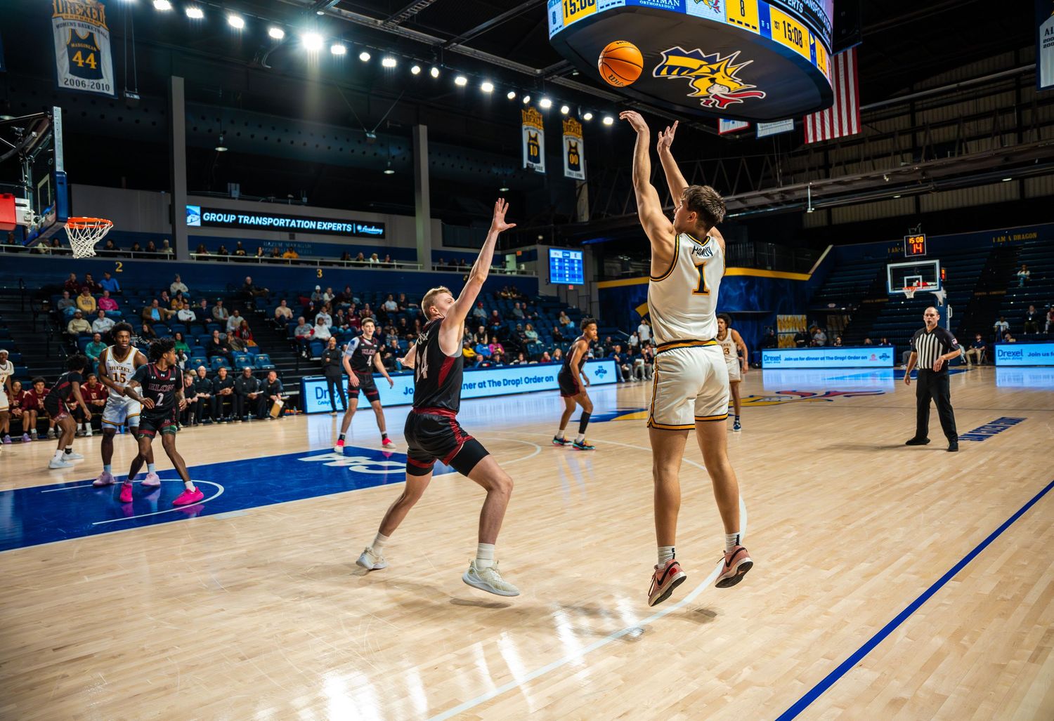 College basketball player shoots jump shot over defender during competitive university arena game.
