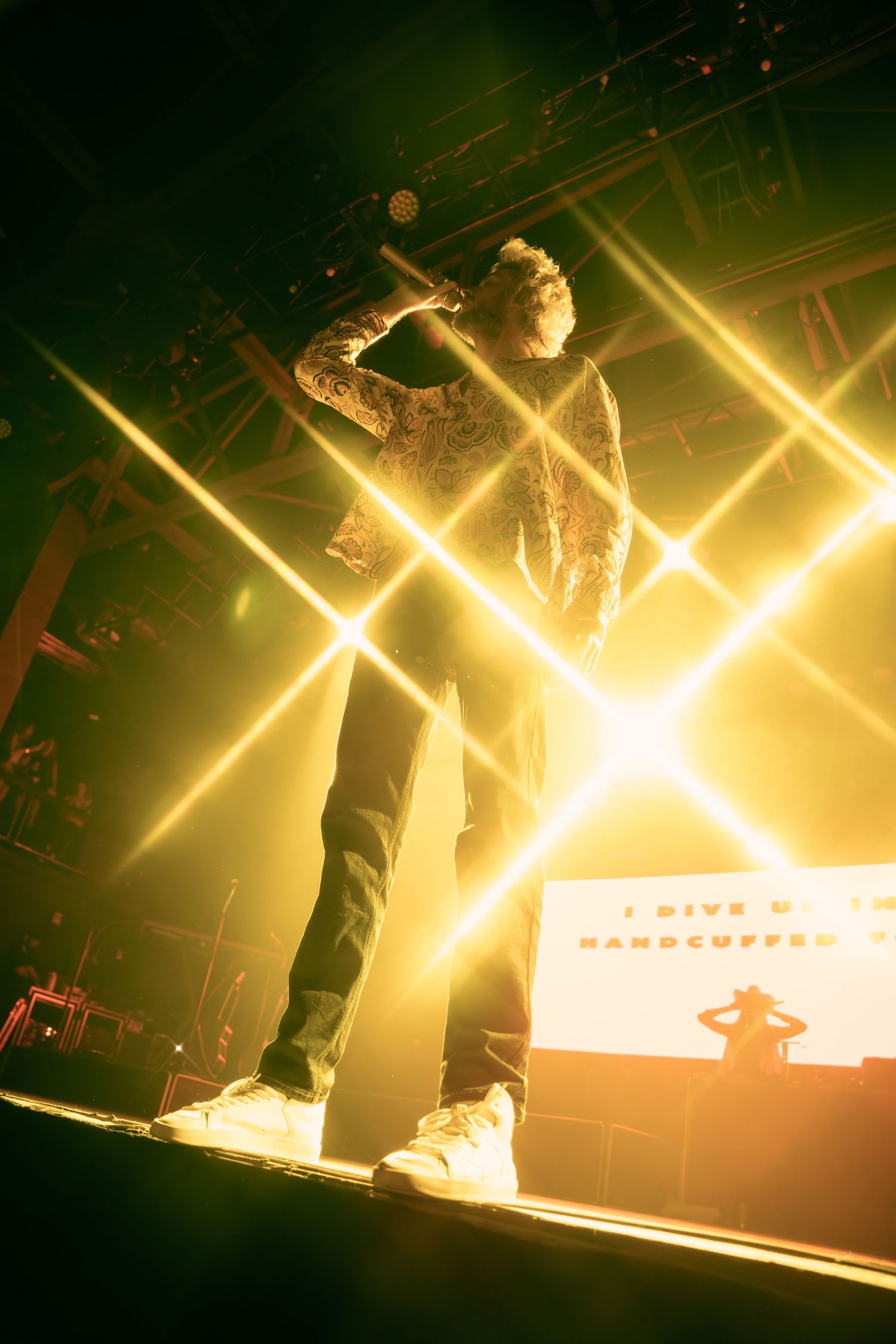 Low-angle shot of performer singing on stage bathed in golden yellow concert lighting.