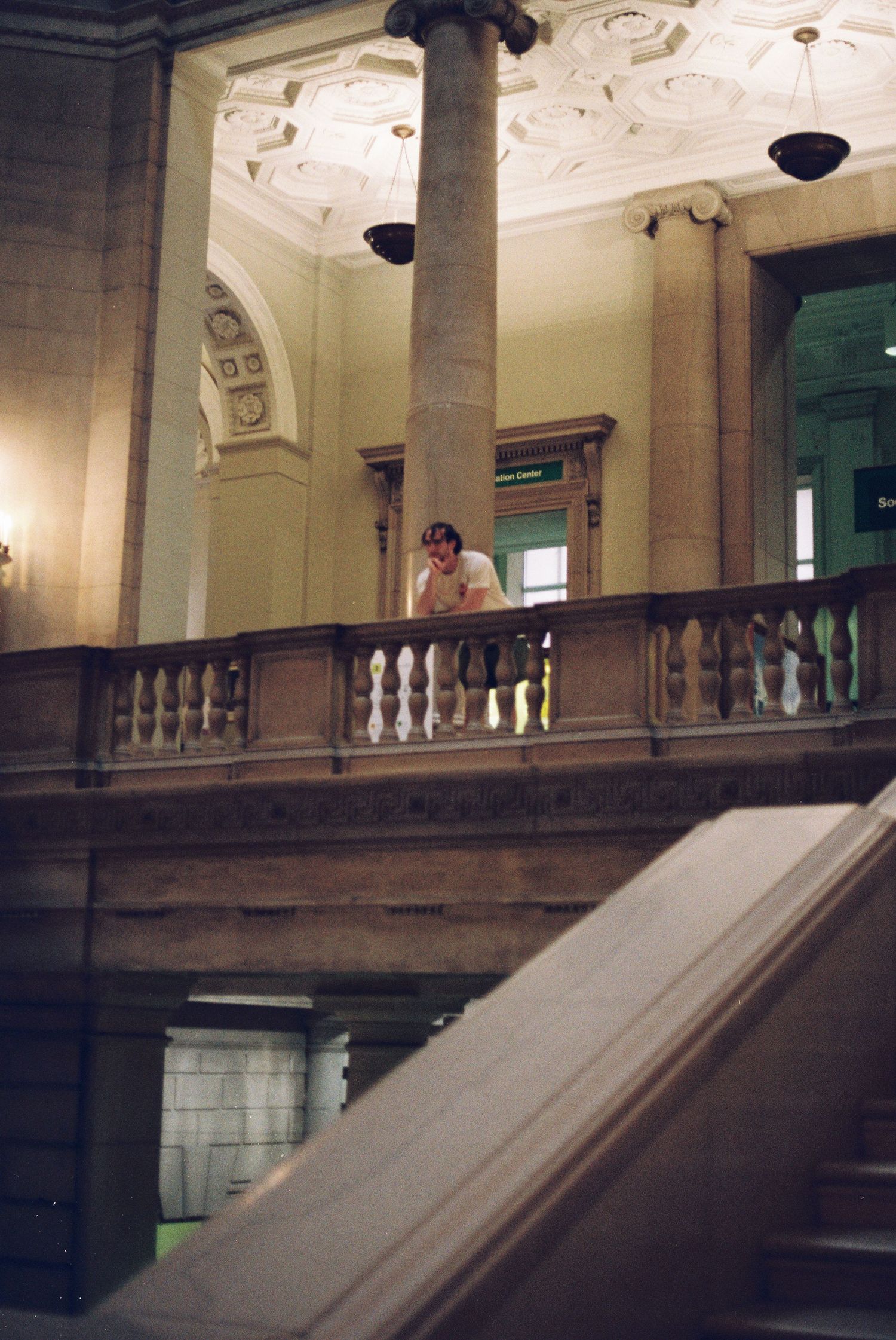 A person leaning on an ornate stone balcony railing inside a grand historic building interior.