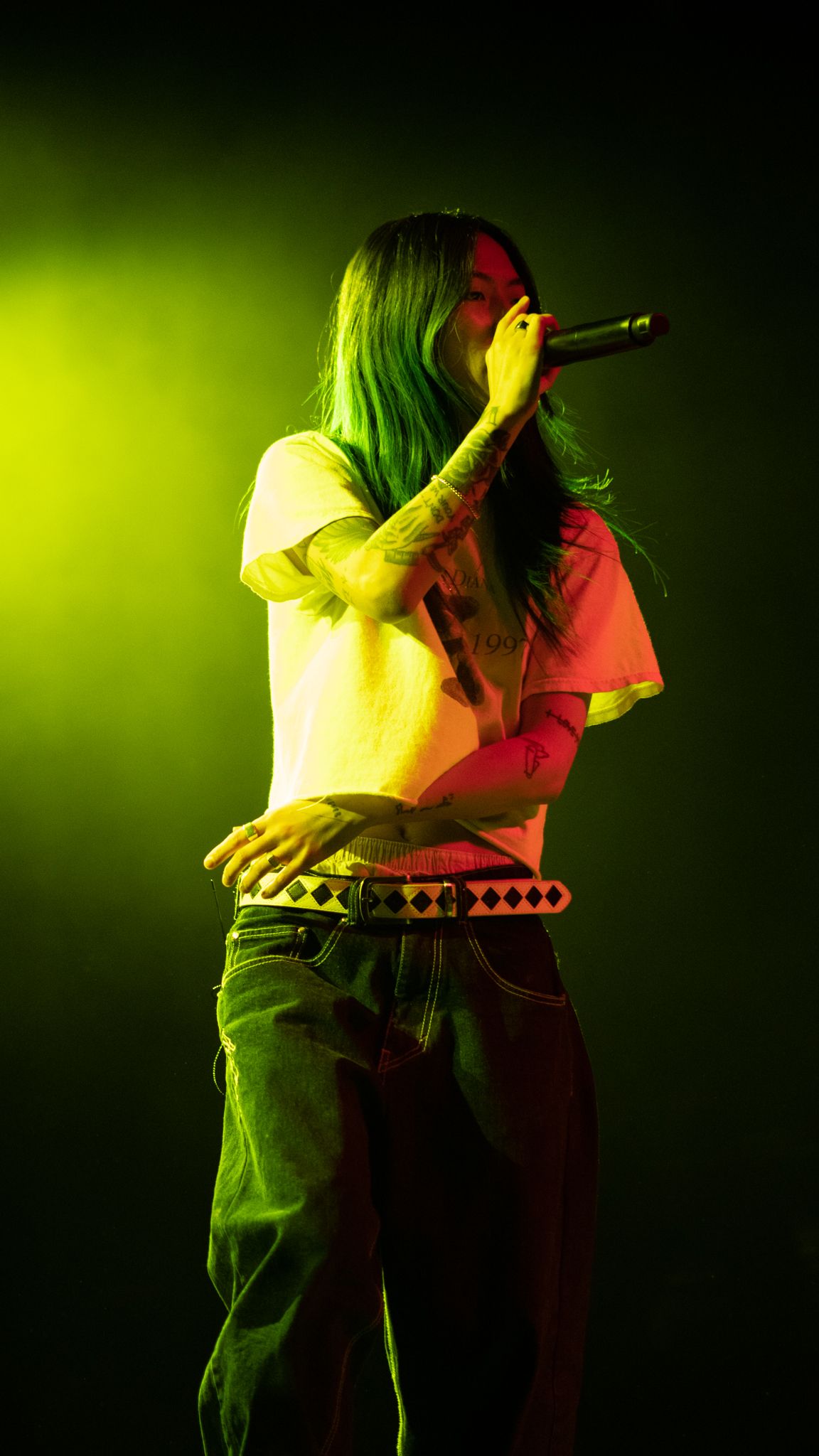 Singer performing on stage under green and yellow stage lighting while holding a microphone.