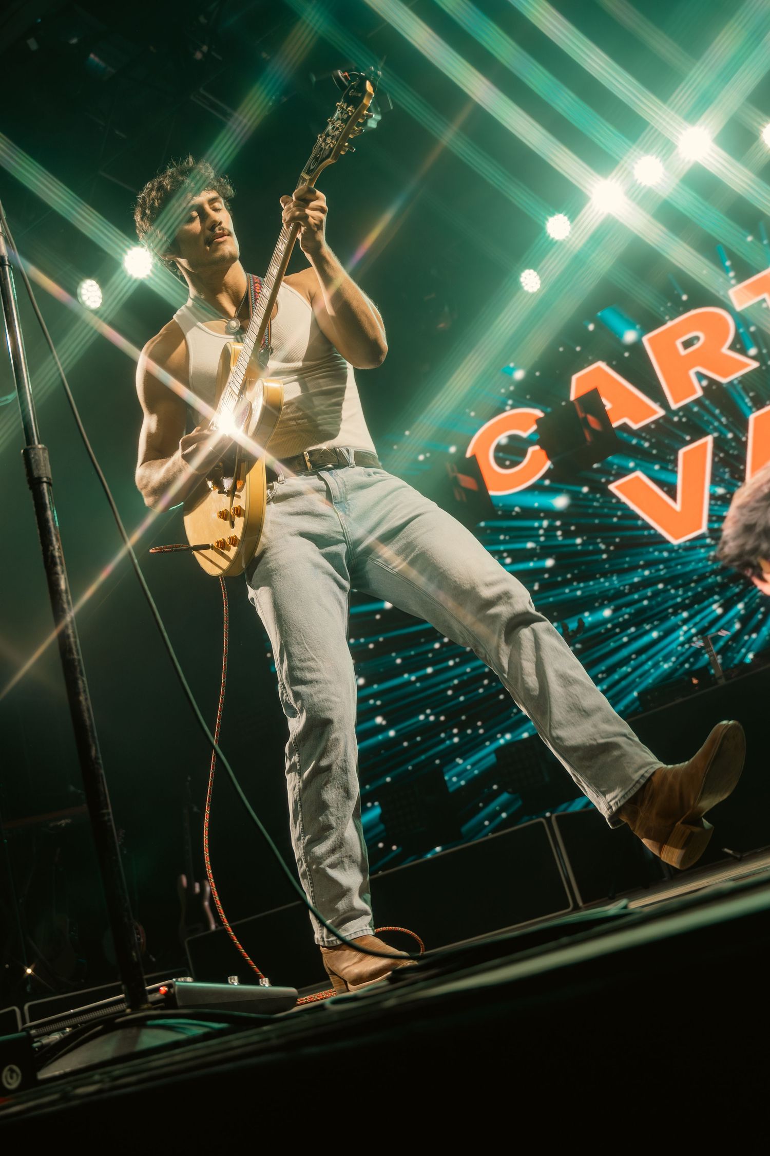 Guitarist performs energetically on stage with dramatic stage lighting at Carter Vail concert.