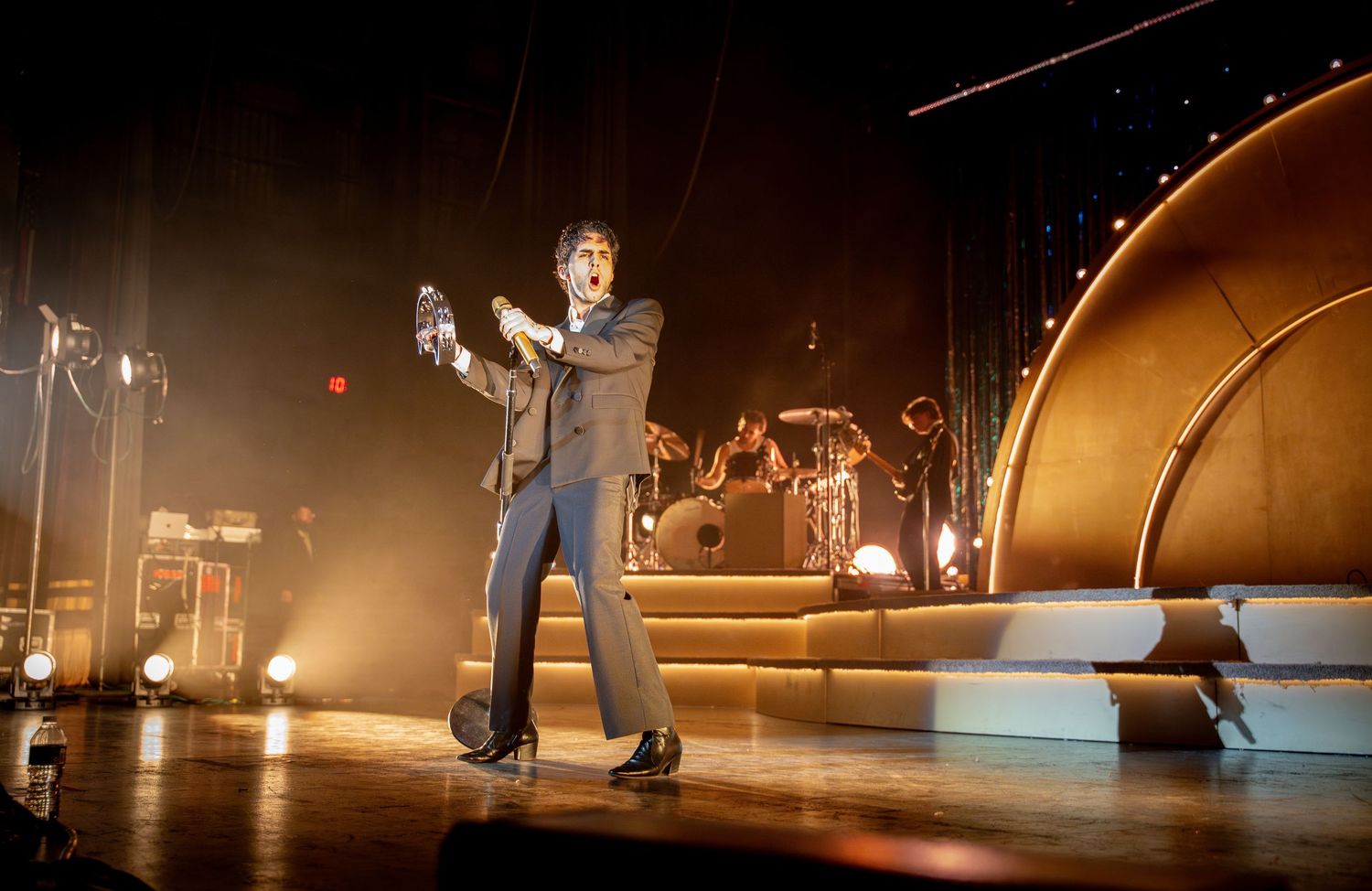 Performer in a suit dancing energetically on a dramatic stage with golden backdrop and band setup.