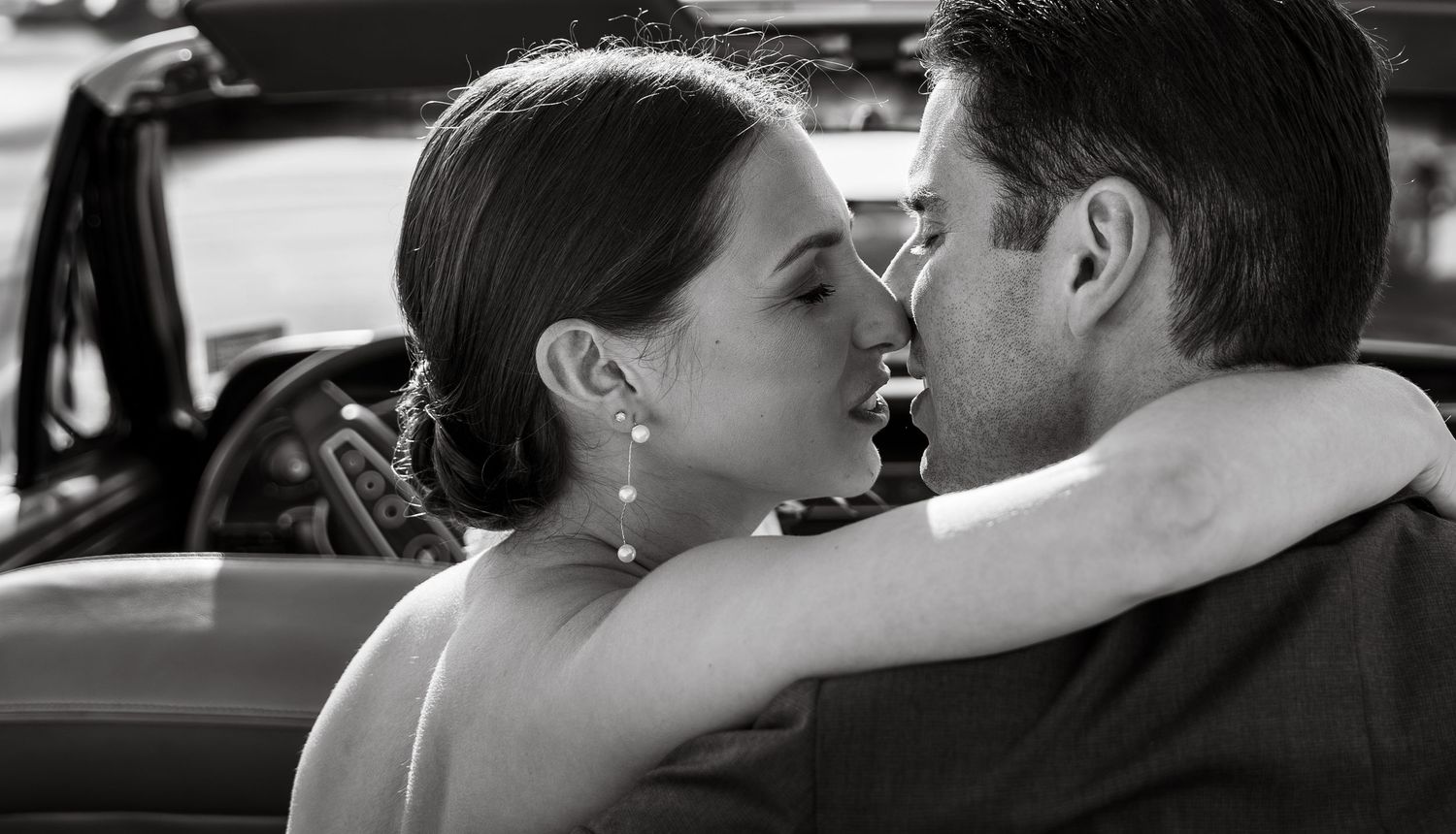Romantic black and white photo of bride and groom sharing an intimate moment in a vintage car.