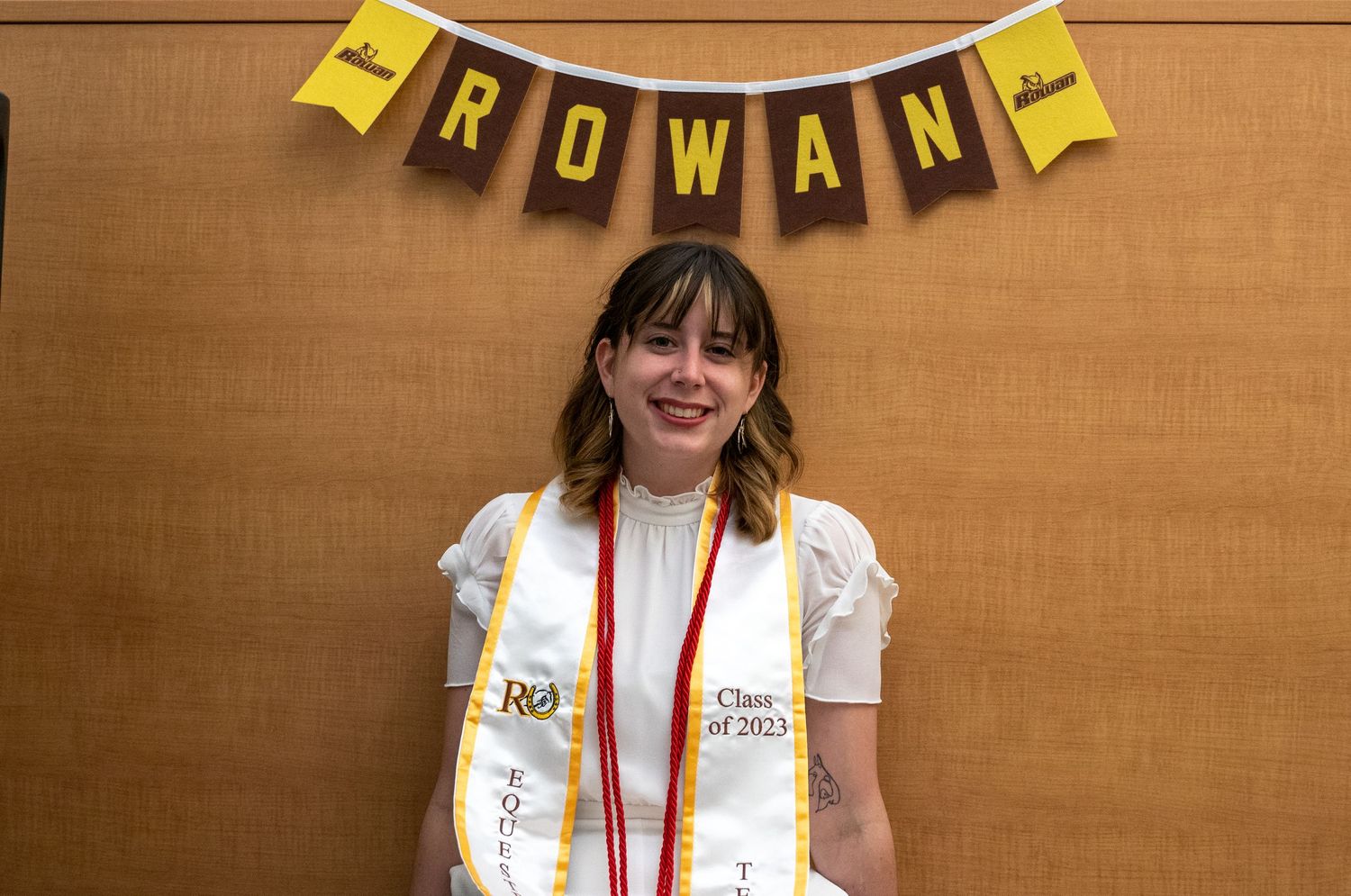 Smiling graduate wearing a stole posing under a Rowan University Class of 2023 banner.