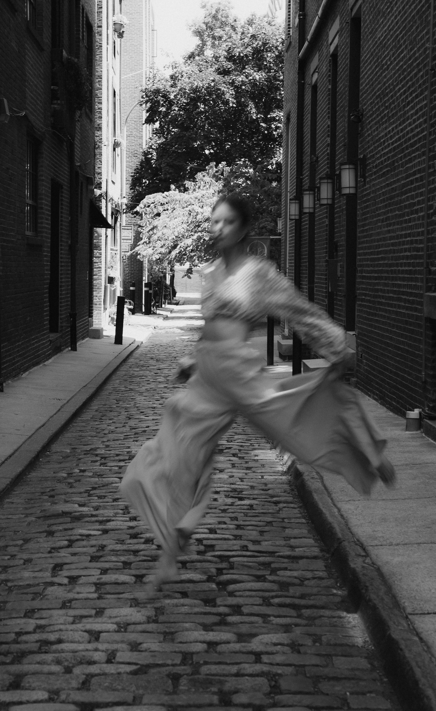Black and white motion blur photo of person running down historic cobblestone alley.