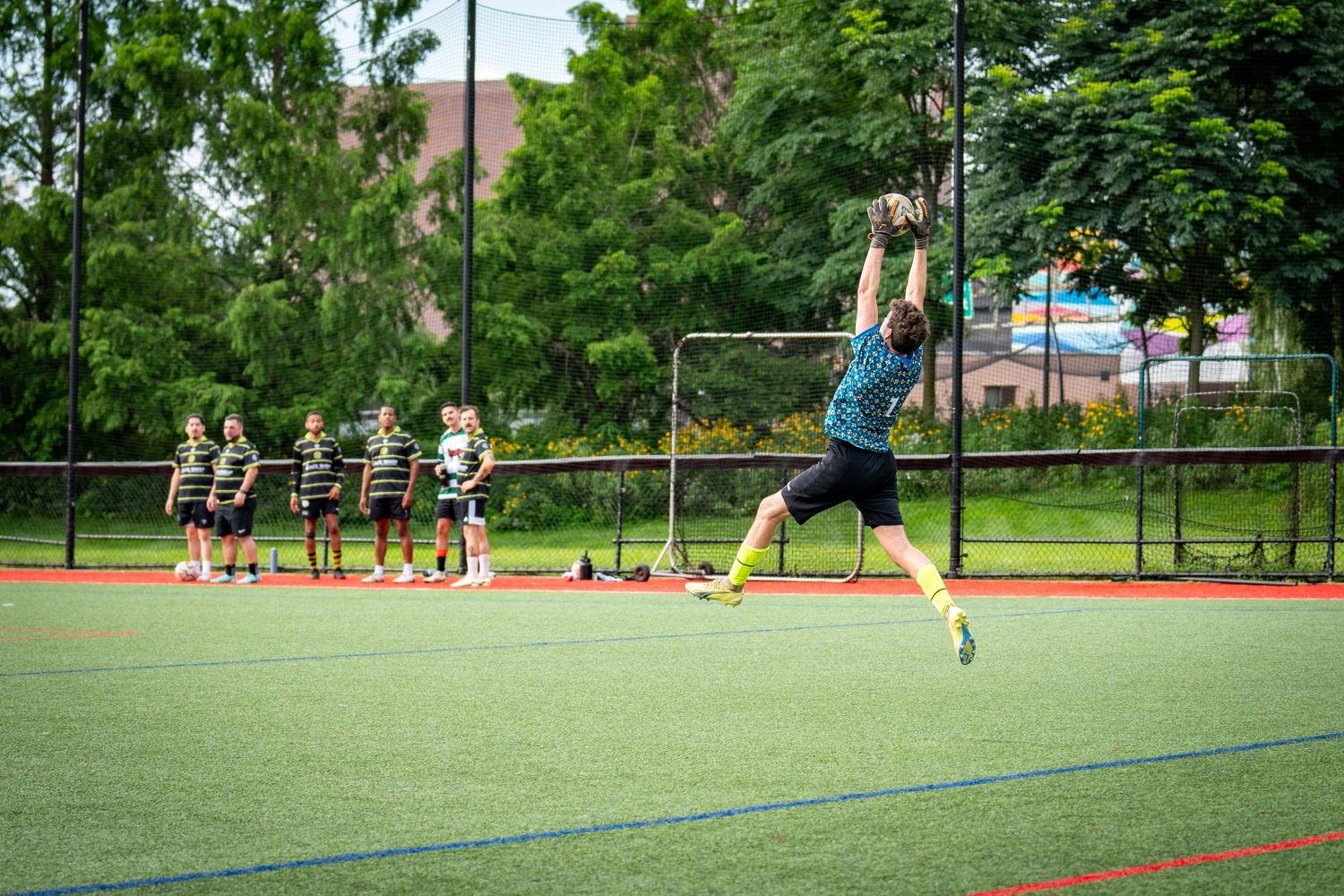 Athlete jumping to catch a ball on an outdoor turf field with teammates watching in background.