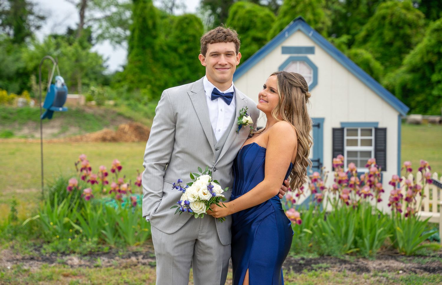 Young couple poses together in formal attire at a garden prom photo shoot.