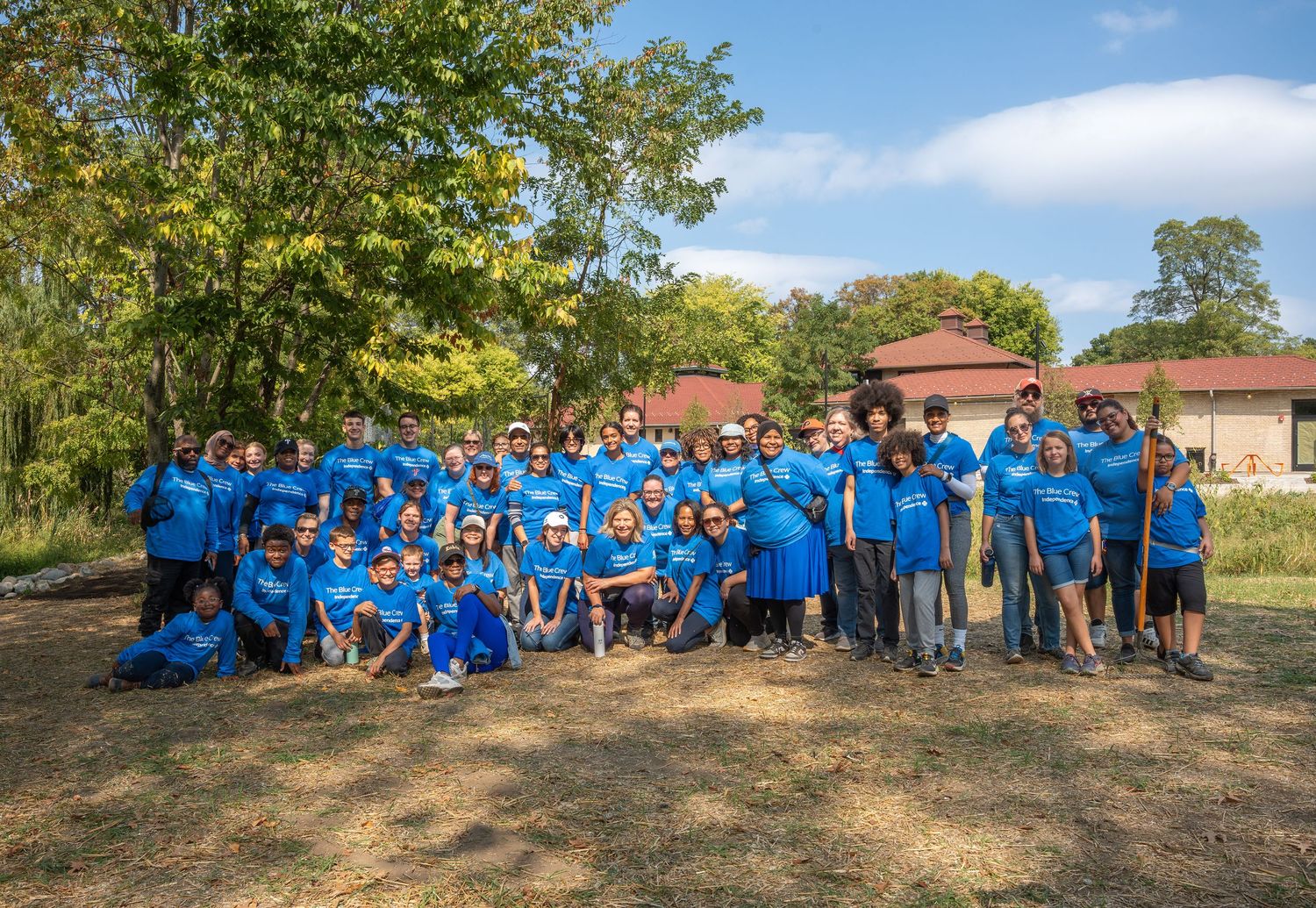 Large group of volunteers in blue shirts posing outdoors near trees during a community service event.