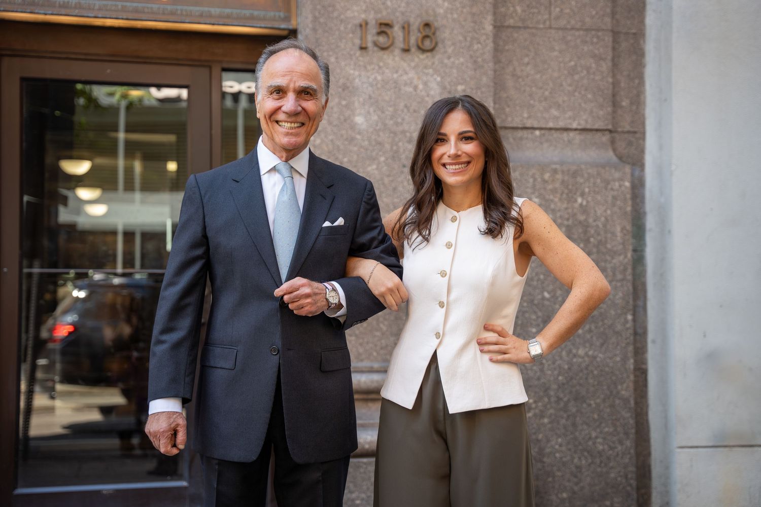 Man and woman in professional attire smiling outside a building entrance numbered 1518.