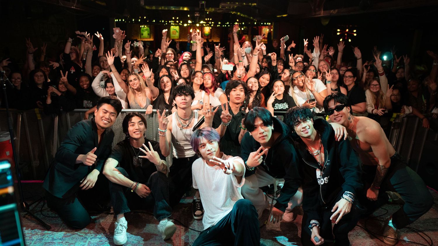 Group photo of band members and fans celebrating together on stage after a live concert performance.