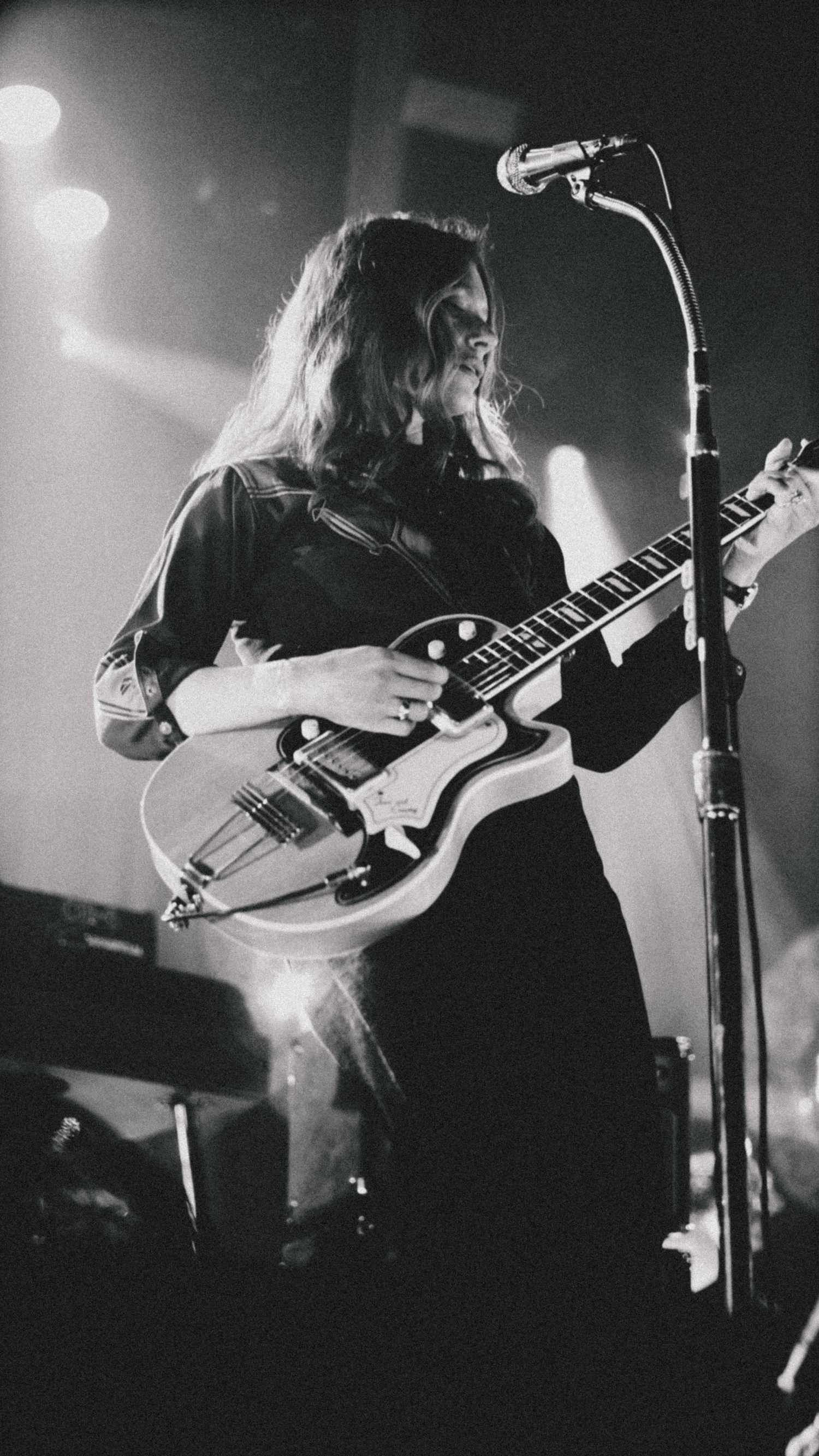 Black and white photo of a long-haired guitarist performing on stage with a semi-hollow electric guitar.