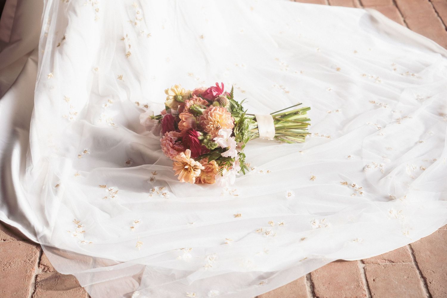 A delicate bridal bouquet of colorful wildflowers rests on a white embroidered wedding veil.